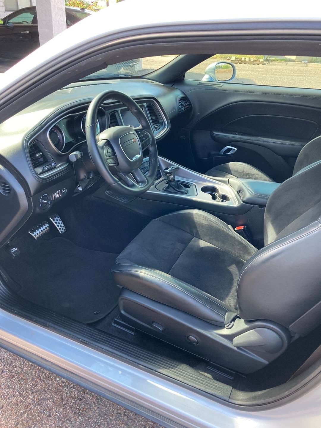 Car interior with black seats, steering wheel, and dashboard, viewed from the open driver’s door