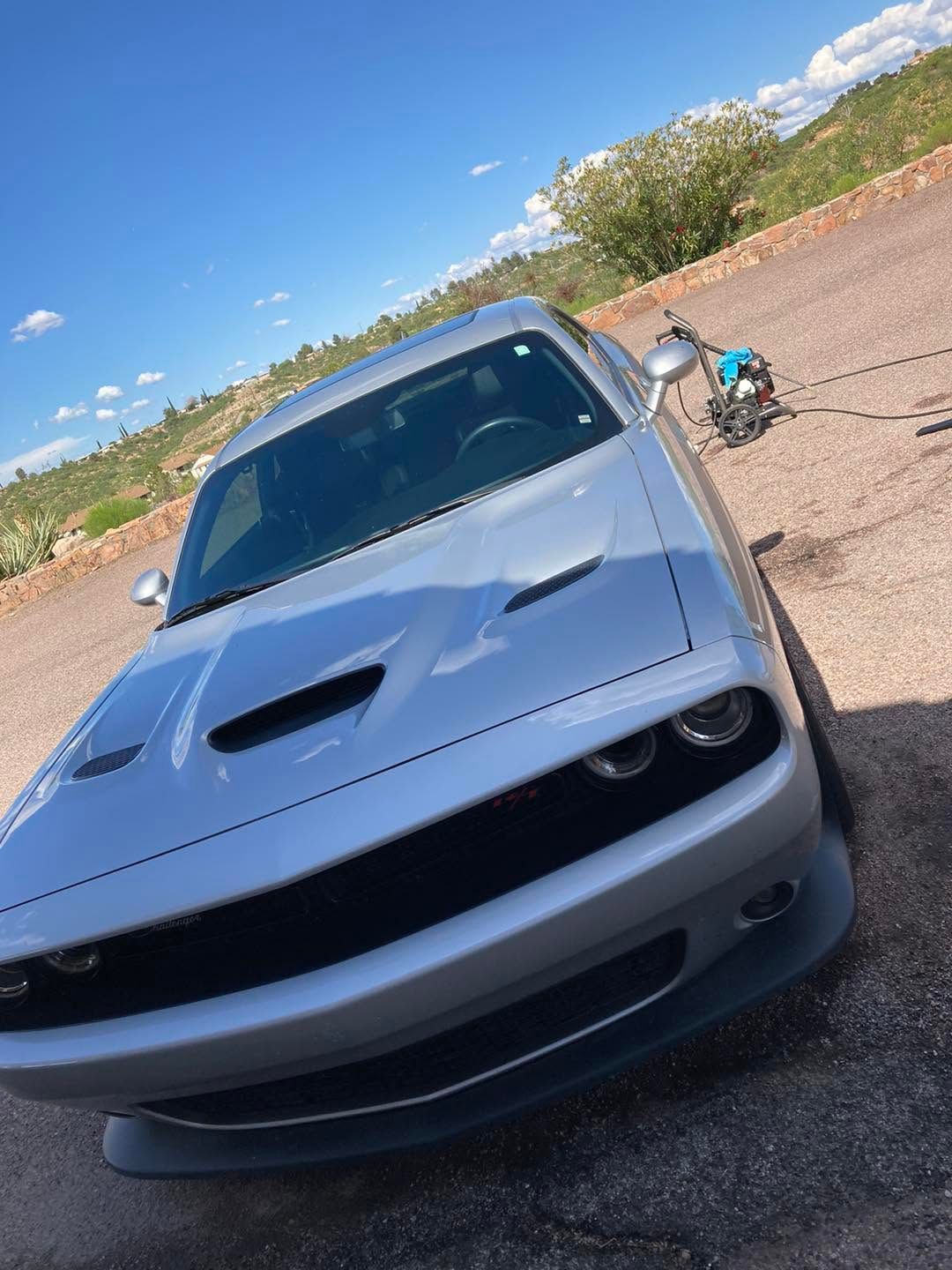 Gray sports car parked on a roadside under a blue sky, angled toward the camera.