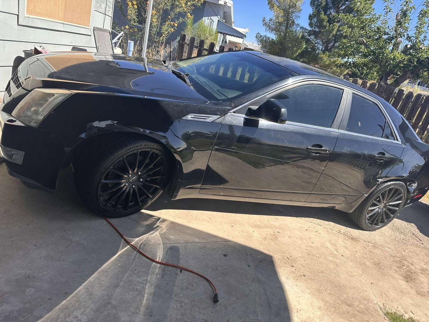 Black sedan with front-end damage parked on a driveway in daylight