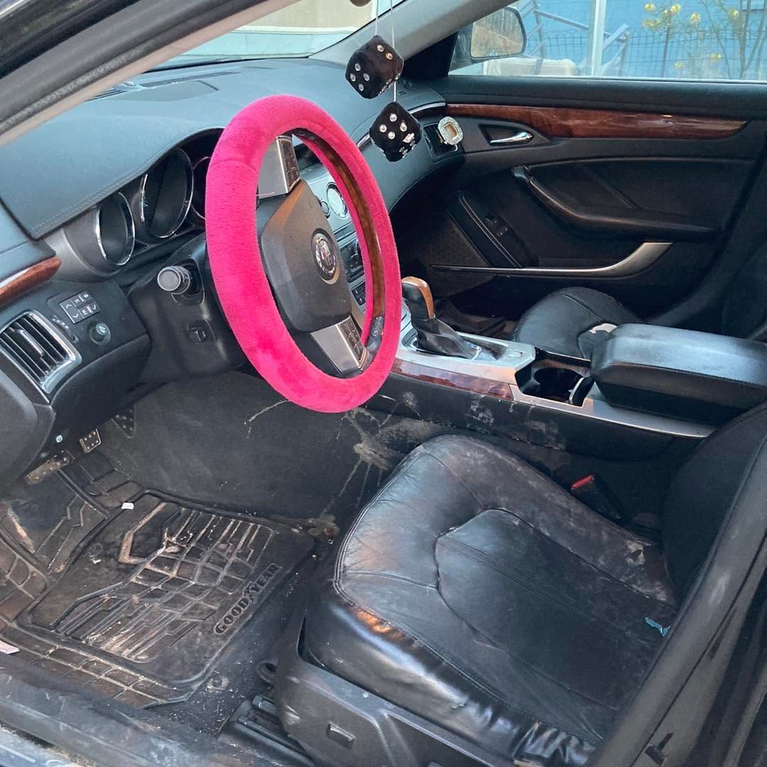 Messy car interior with pink steering wheel cover and worn seats, viewed from the driver’s side