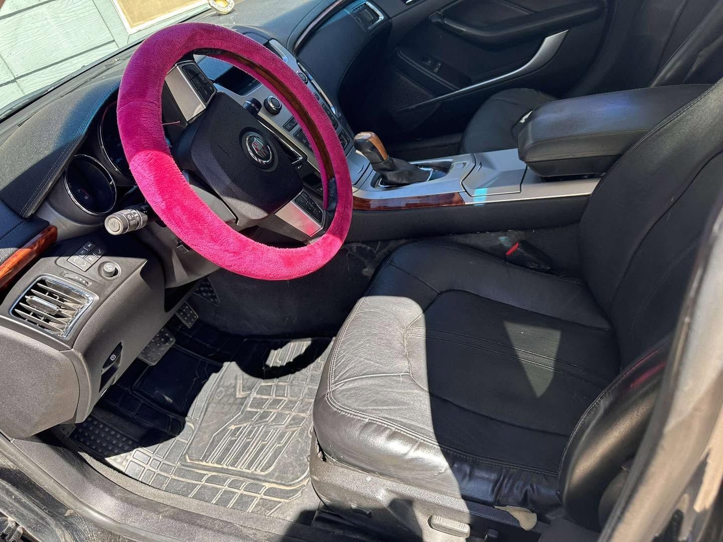 Car interior with a bright pink steering wheel cover and black leather seats, viewed from the driver’s side.