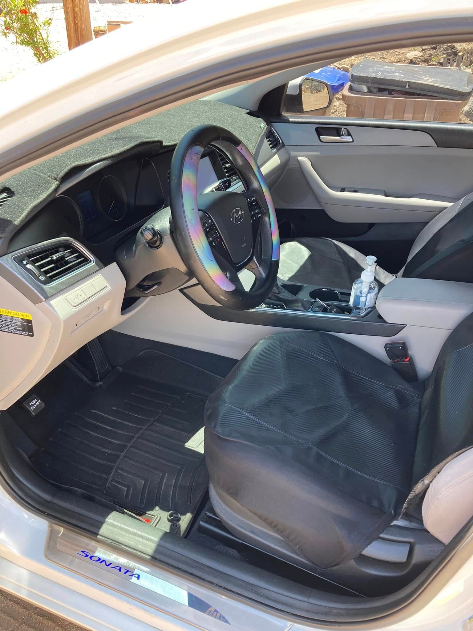 Open car door showing driver’s seat, steering wheel, and front interior with black seats and tan dashboard.