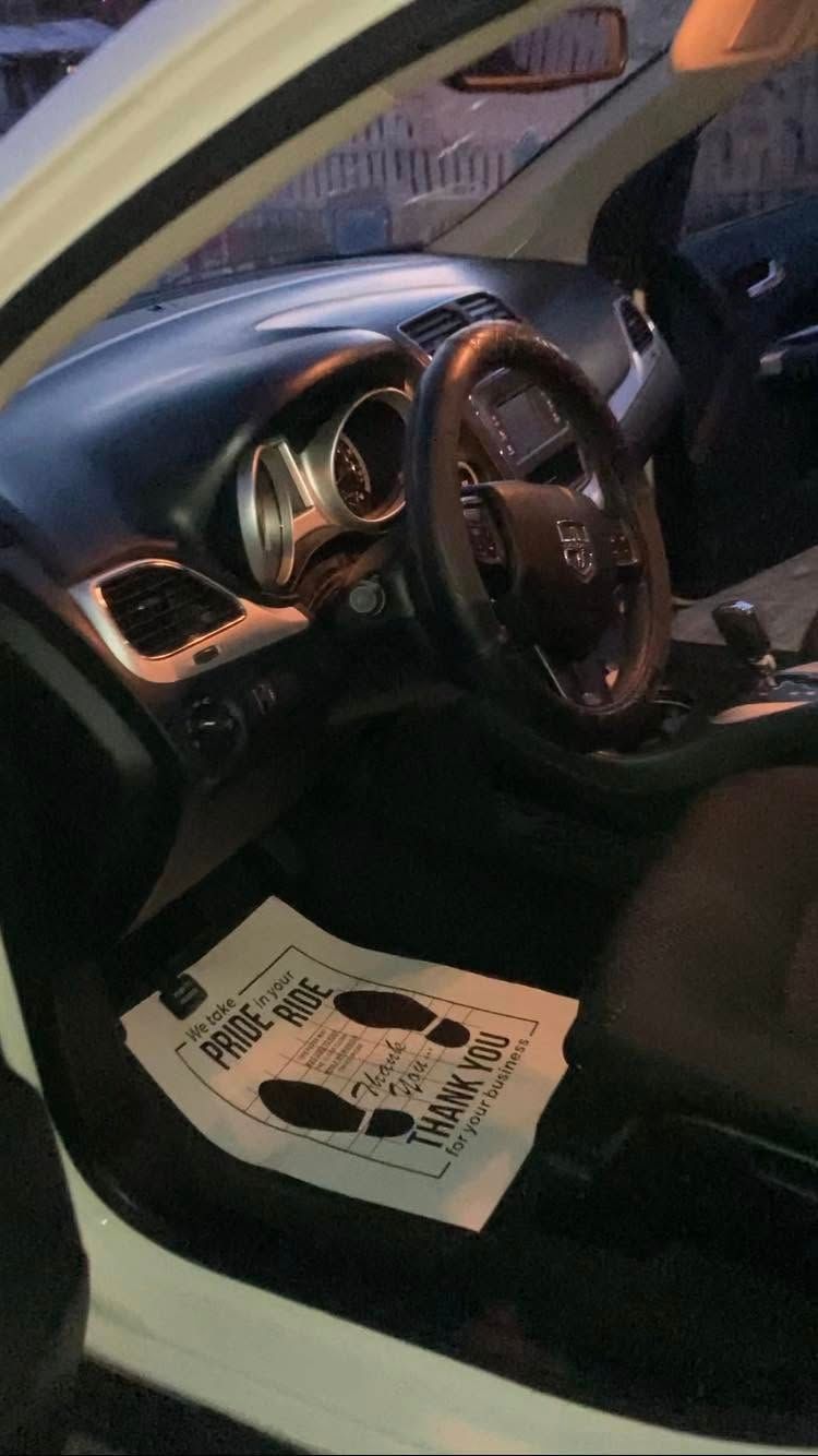 Car interior with steering wheel and dashboard, driver’s door open, papers on the seat floor area