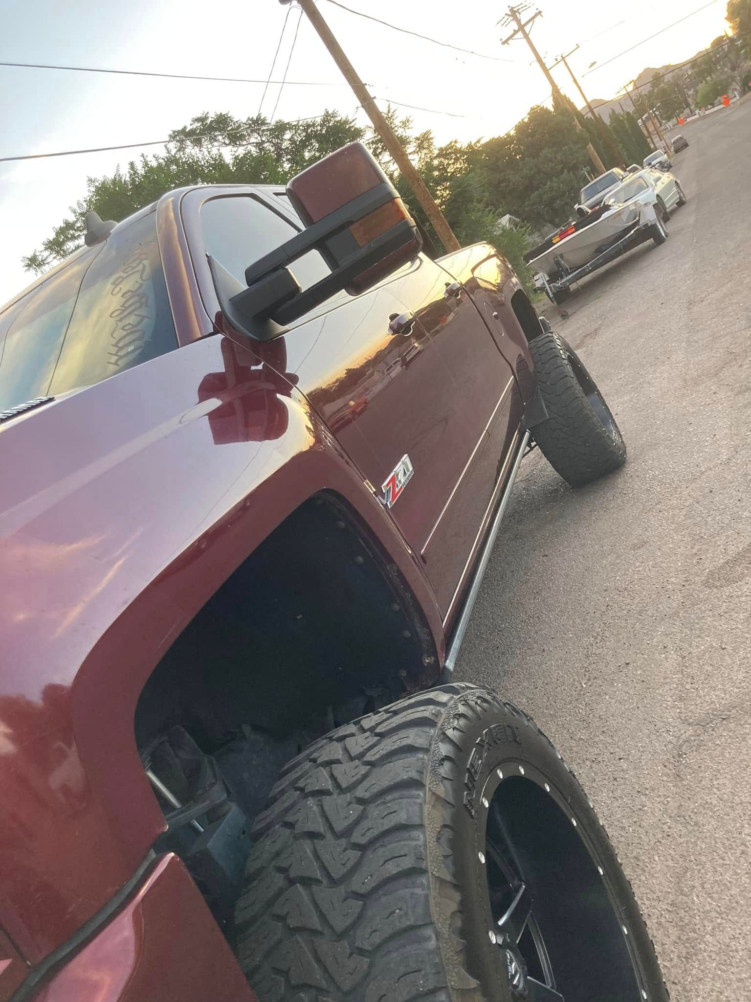 Maroon lifted pickup truck parked on a gravel roadside at sunset, angled view of front wheel and mirror