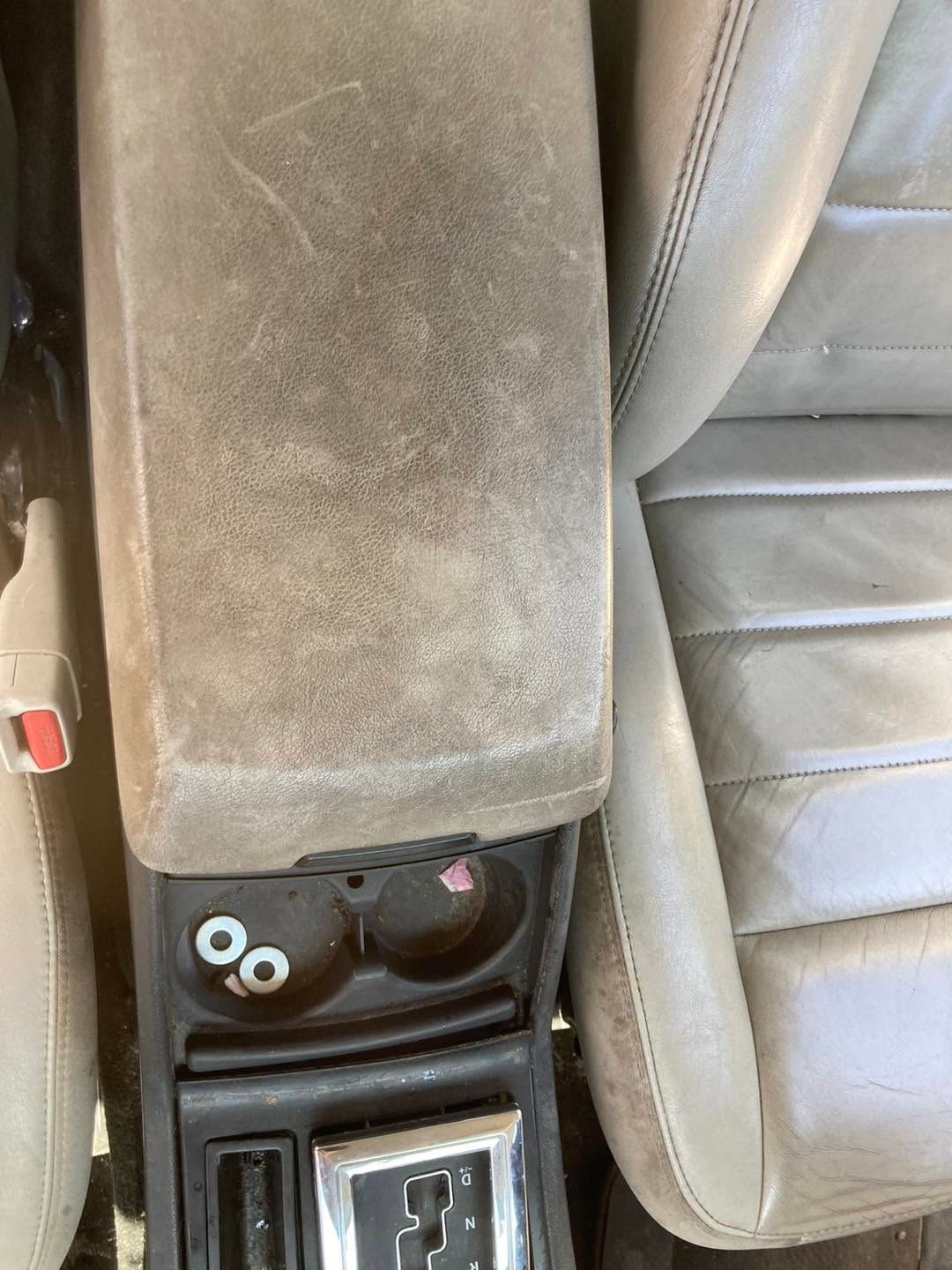 Car center console with dusty beige armrest, cupholders, and gear shift between two seats