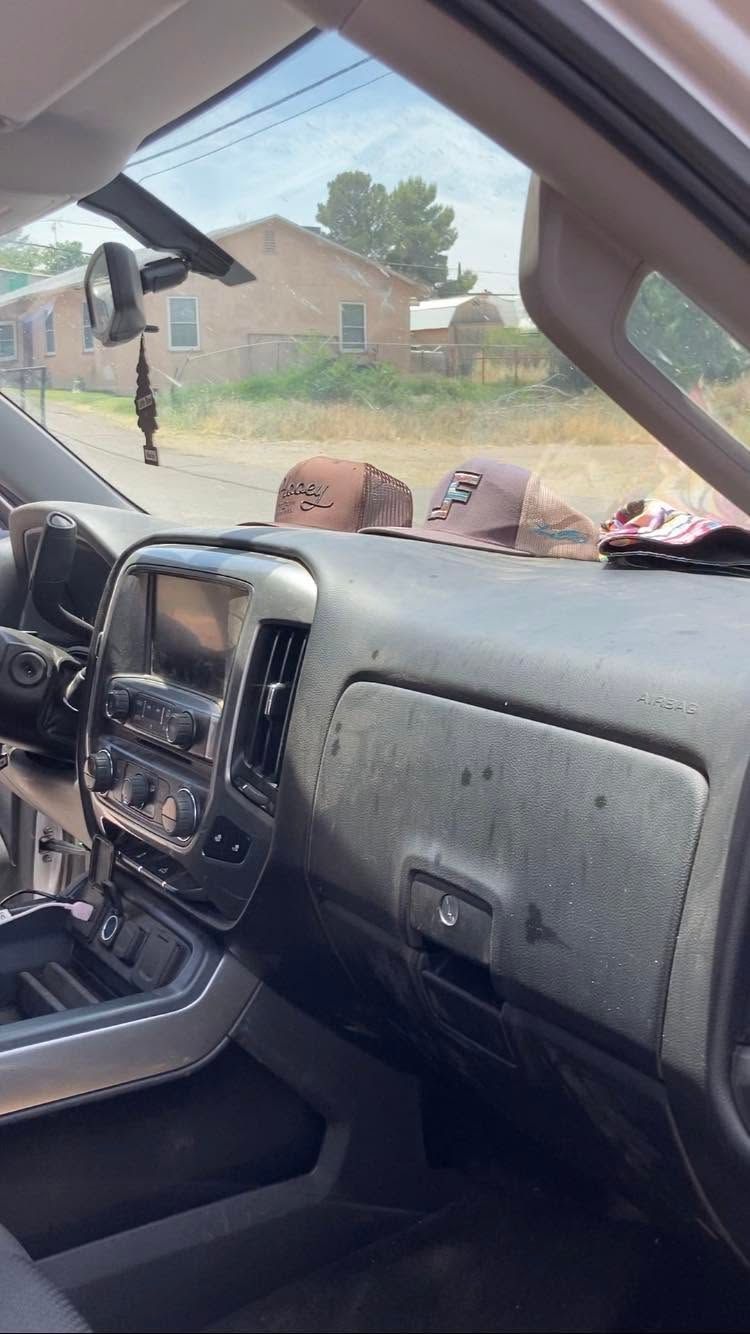 View from a car interior through the windshield, with a dashboard and a house visible outside.