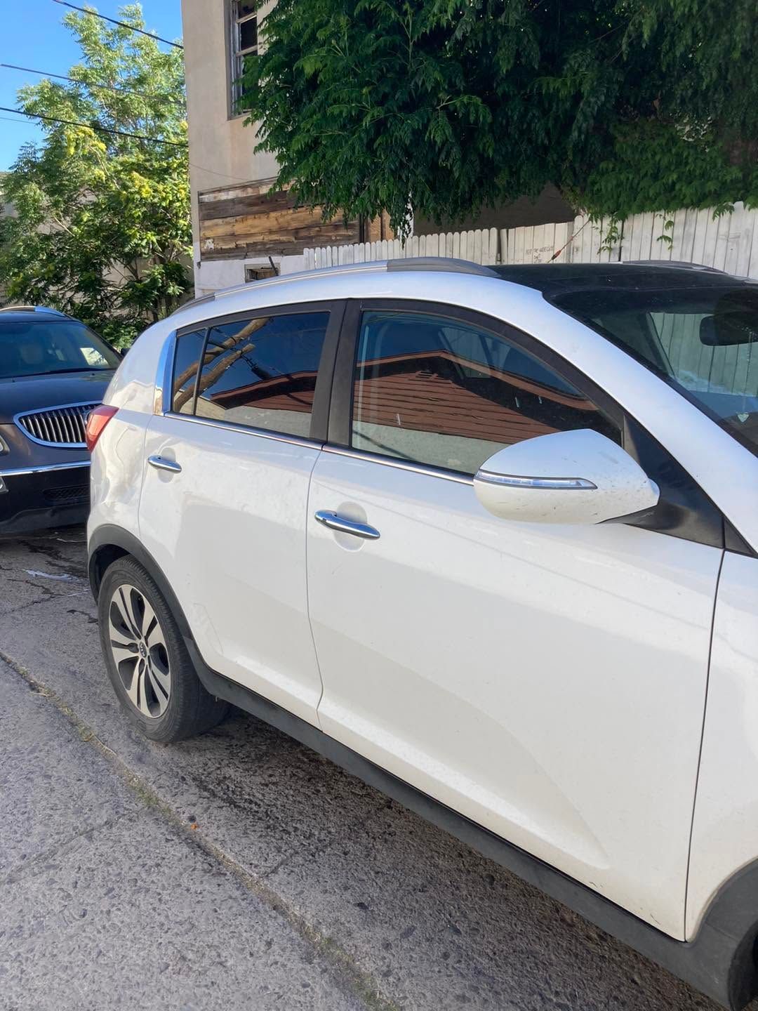 White compact SUV parked along a street beside a building and tree.