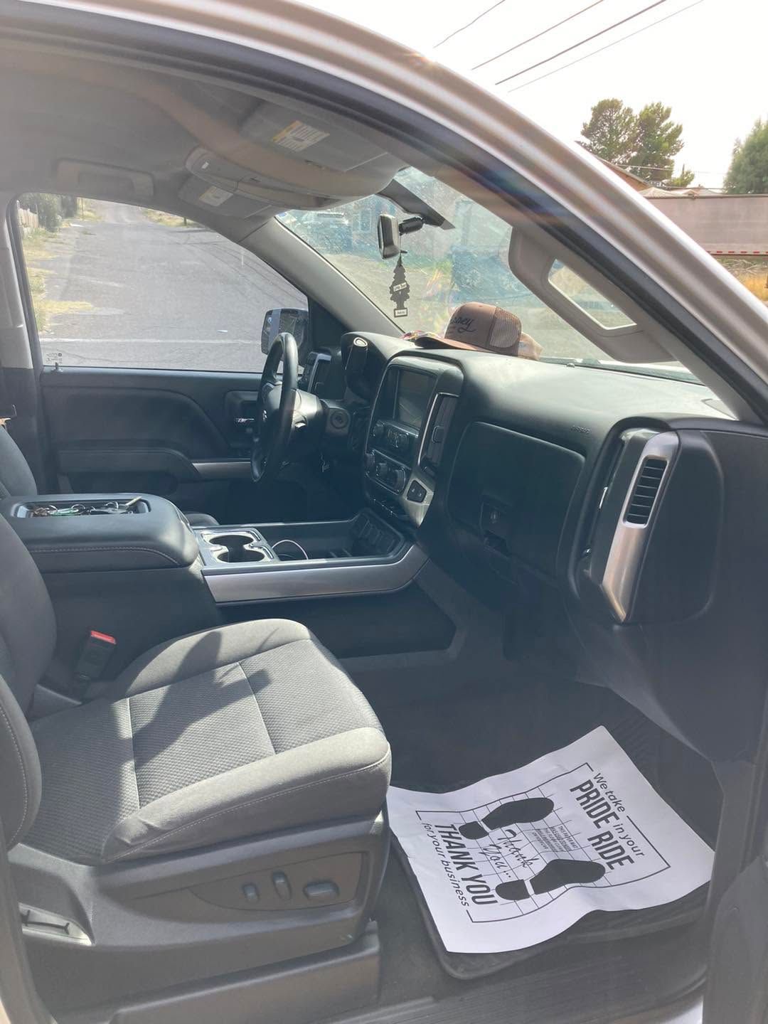 Interior of a parked car with the driver door open, showing black seats, dashboard, and a paper floor mat.
