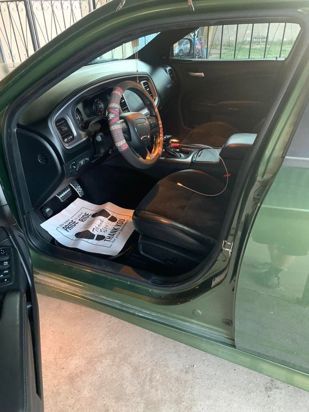 Open car door showing black leather interior and steering wheel, with paper floor mats on the driver’s seat area