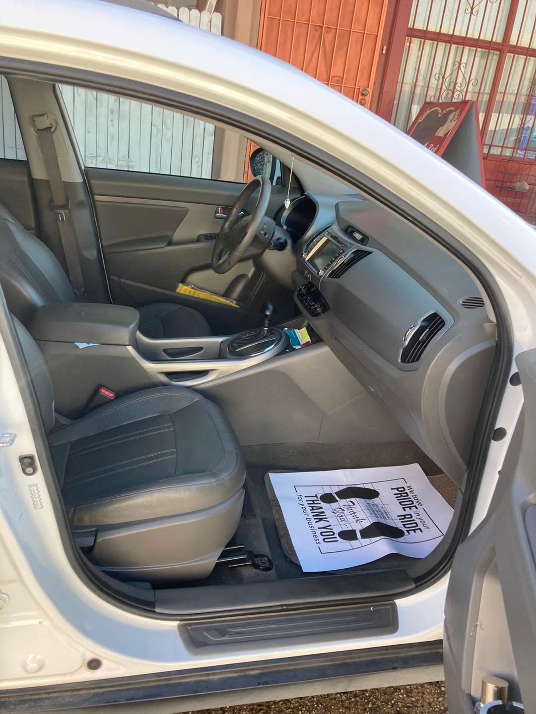 Open car door showing black leather interior, beige dashboard, and floor mat on the passenger side.