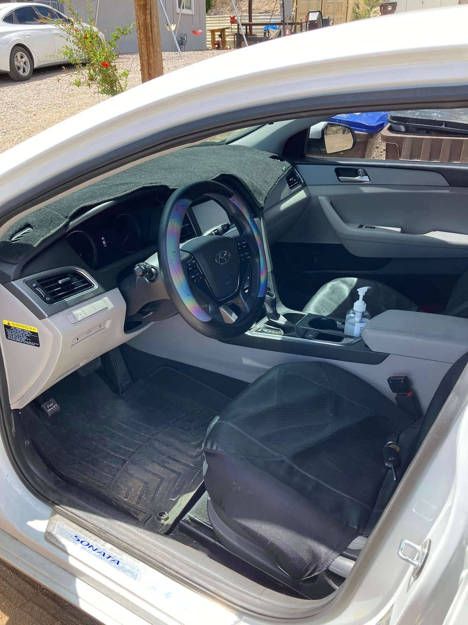 White car interior with open driver’s door, black seat covers, and a steering wheel cover.