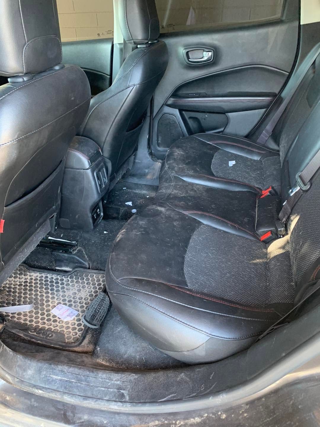 Dirty back seat of a car with black upholstery and visible debris on the floor.