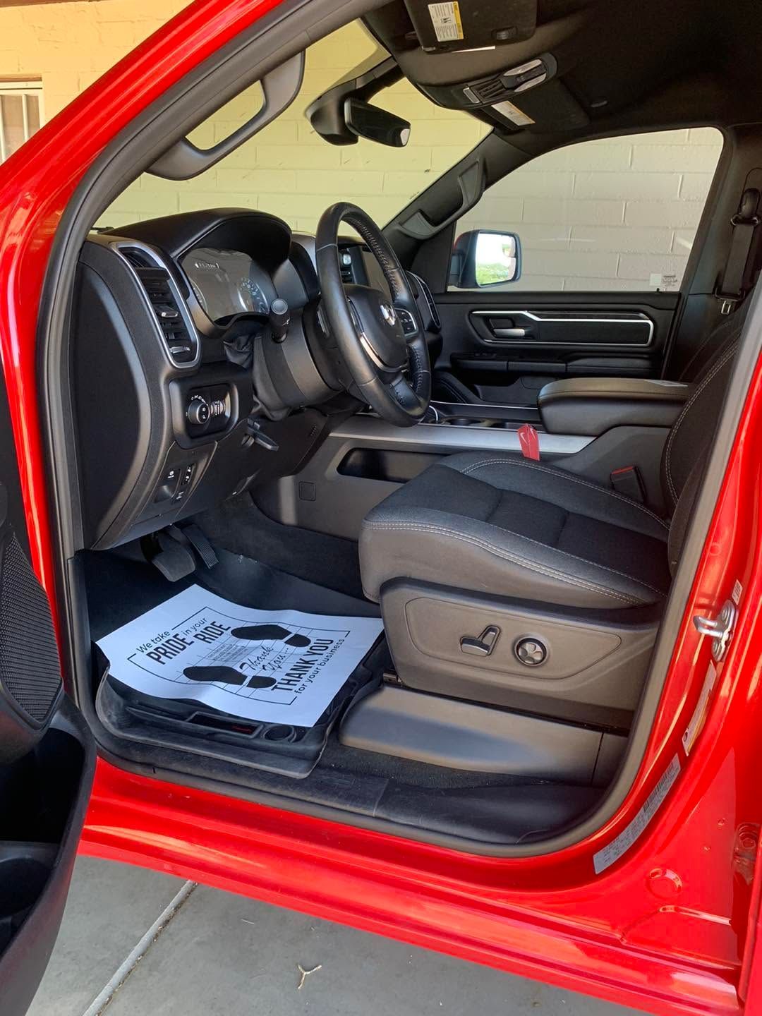Red car interior with open driver door, black seats, steering wheel, and floor mat displayed.