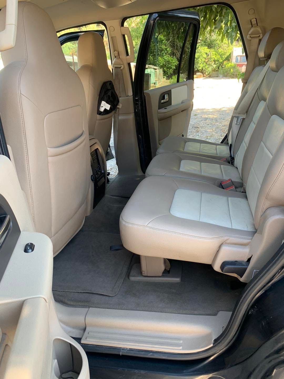 Open SUV interior with beige leather seats and open rear door, sunlight and greenery outside