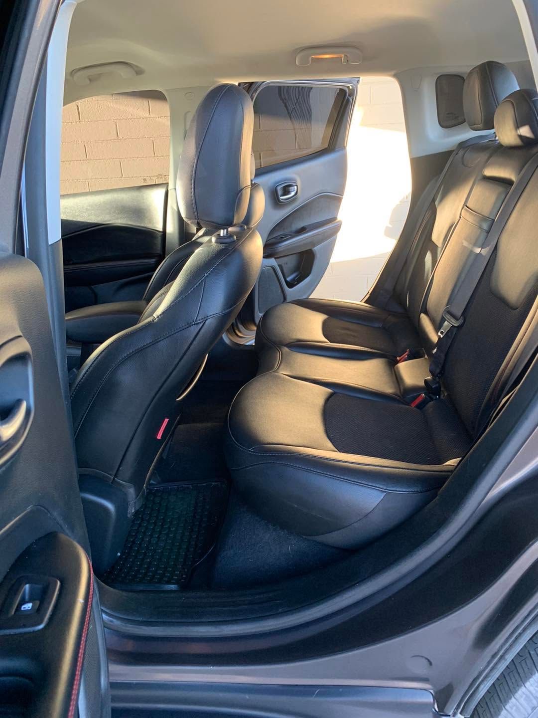 Rear interior of a car with black leather seats and open door, showing the back seat area.