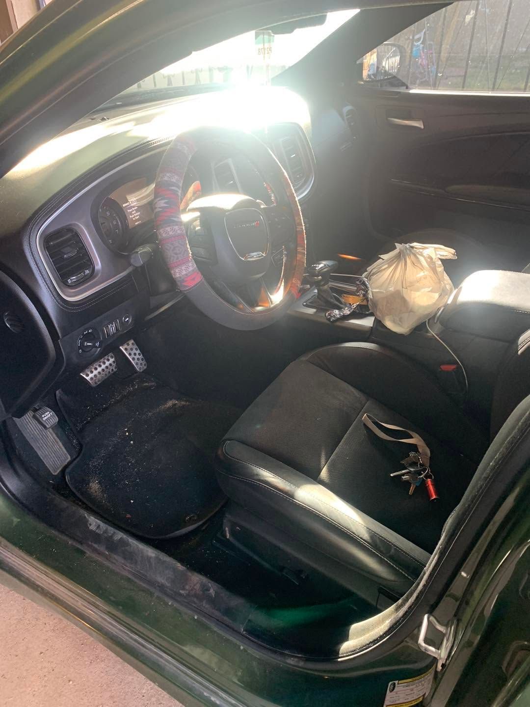 Car interior with black seats and steering wheel, sunlight streaming in through the open driver’s door.