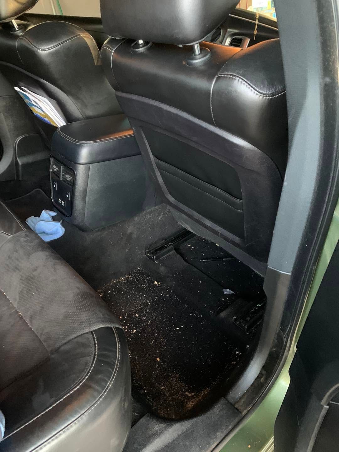 Car interior with black seats and center console, showing a messy floor with scattered debris.