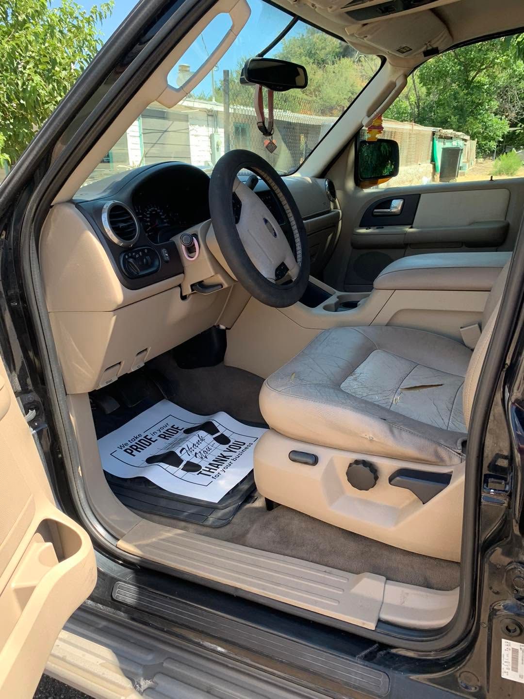 Open car door showing beige interior, steering wheel, front seat, and dashboard in daylight.