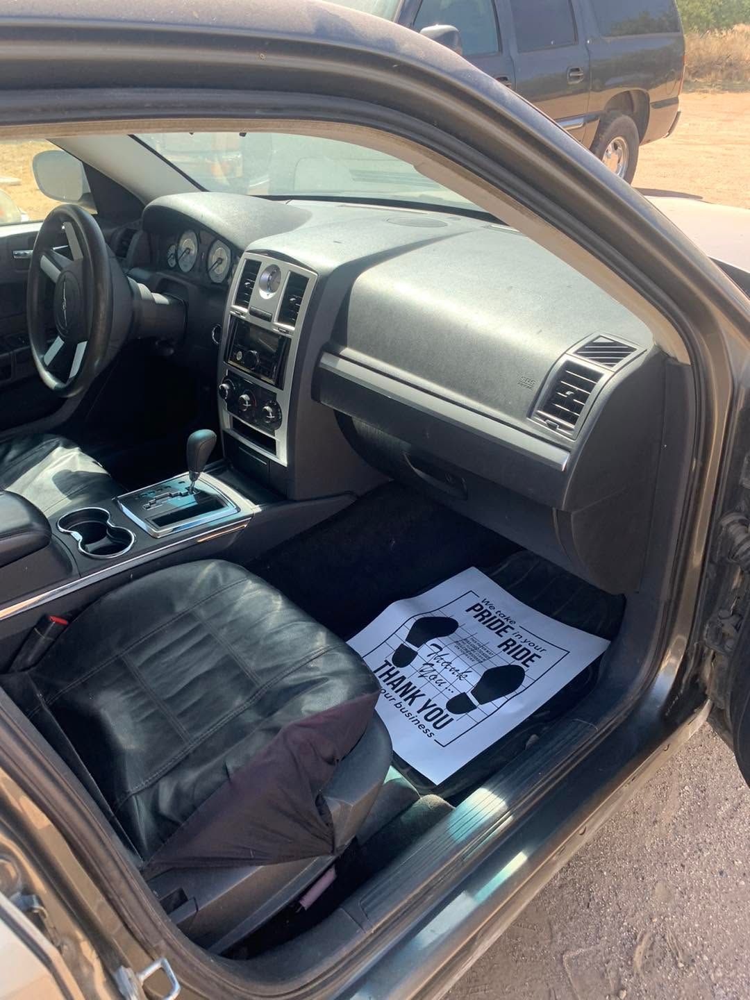 Car interior with black leather seats, dashboard, center console, and a paper floor mat on the passenger side.