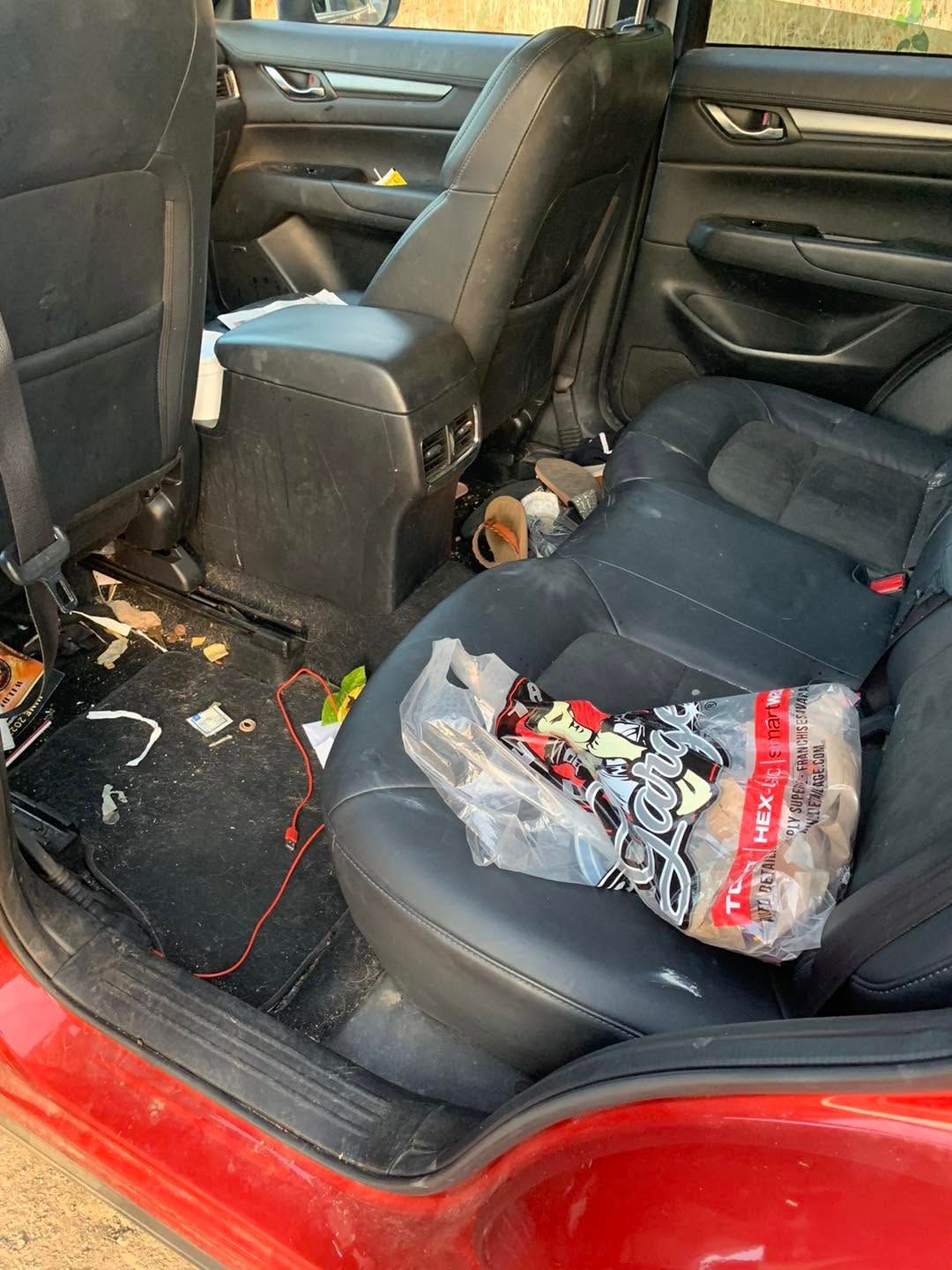 Messy car back seat with trash, a plastic bag, and a red floor mat.