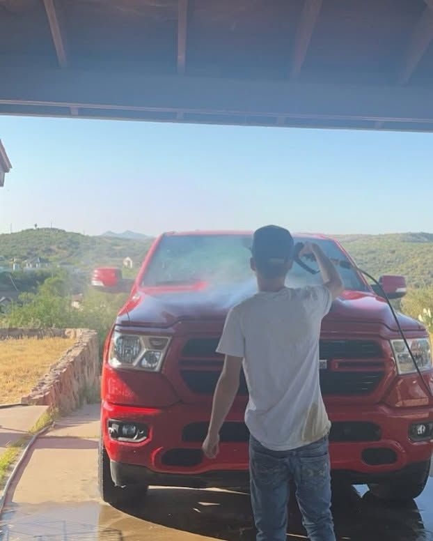 Person facing a red pickup truck under a shaded carport with hills in the background