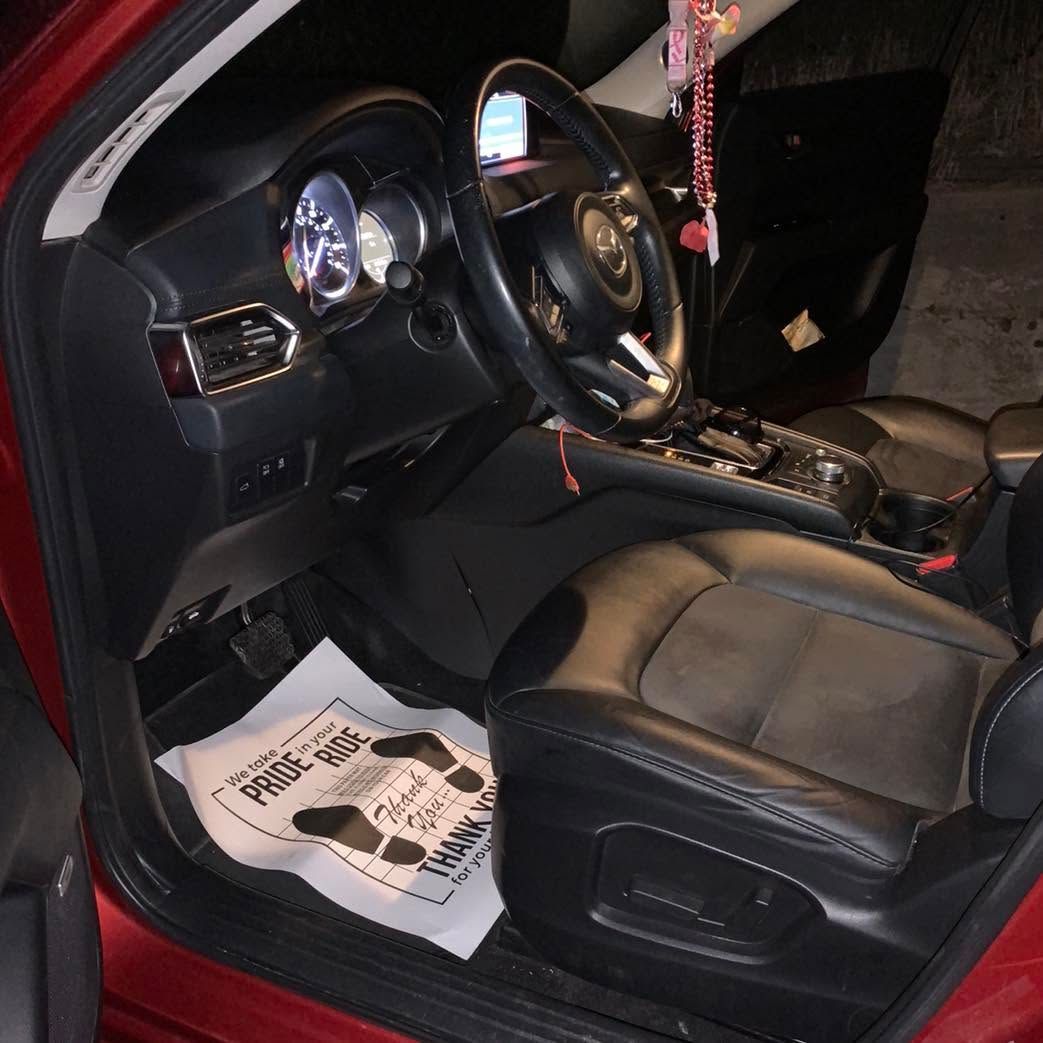Black car interior with leather seats, steering wheel, center console, and papers on the driver-side floor.