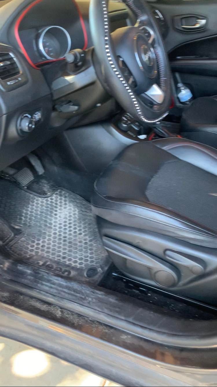 Car interior with black seats, steering wheel, dashboard controls, and a textured floor mat