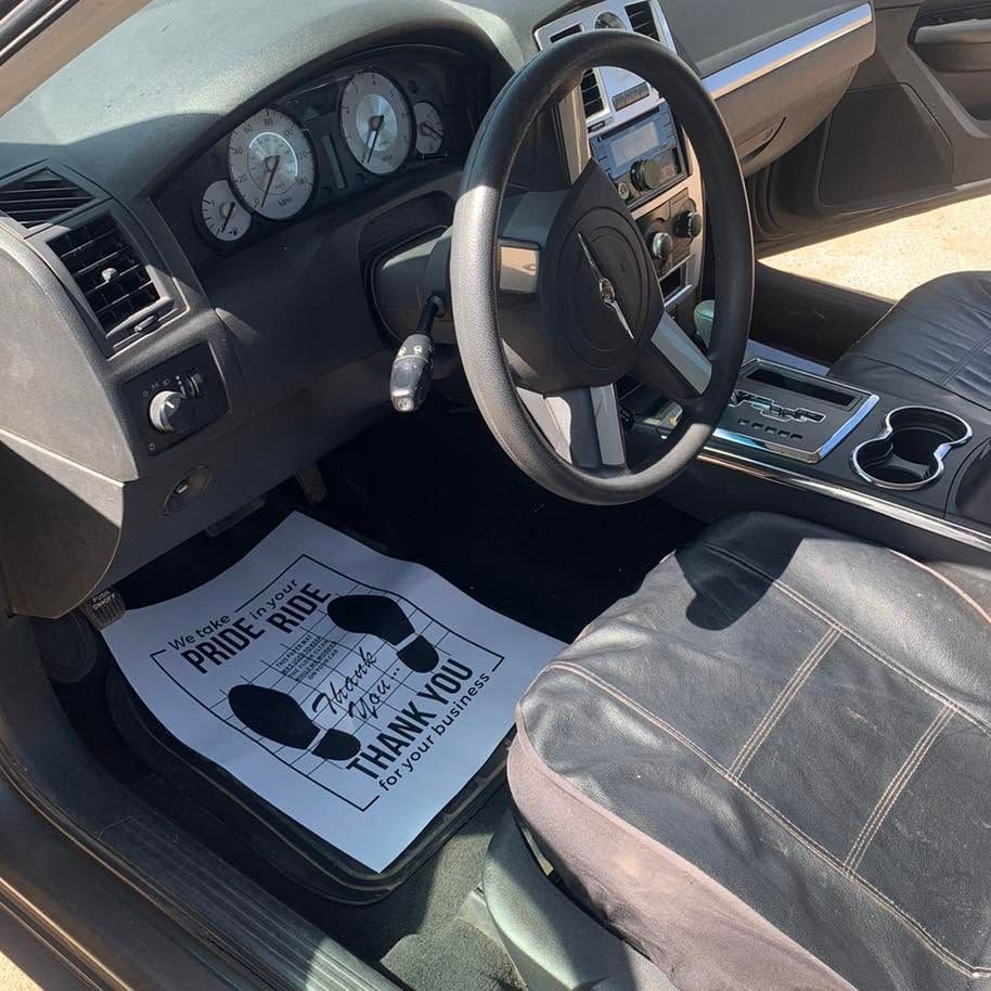 Car interior with black seats, steering wheel, dashboard, and a floor mat reading “I parked like a pro.”