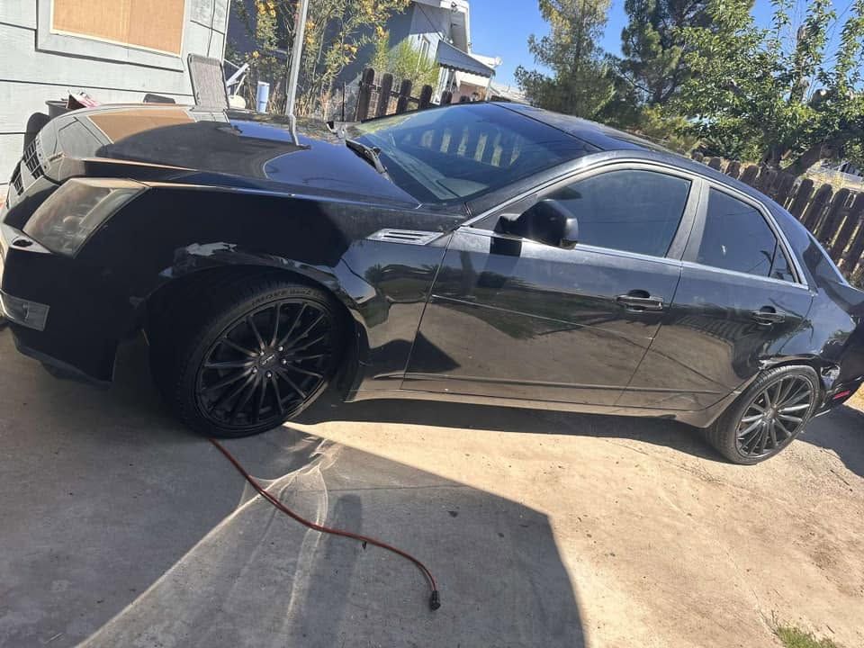 Black sedan parked in a driveway with front-end damage and a loose cable on the ground.