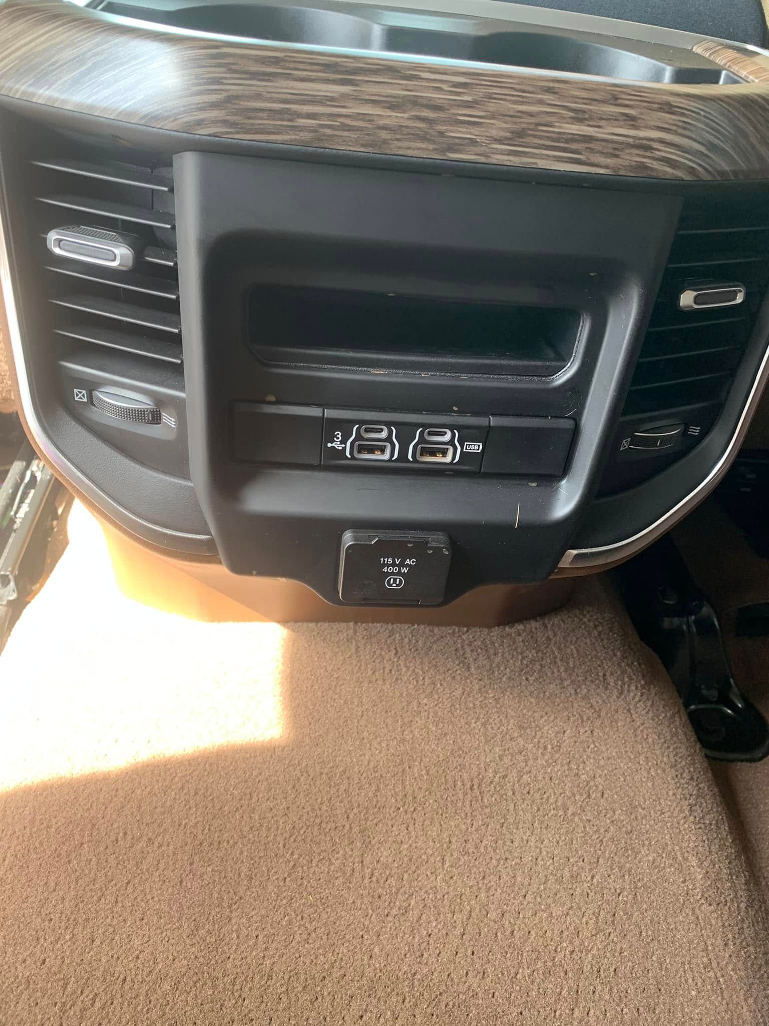 Car dashboard center console with air vents, climate controls, and a power outlet beneath.