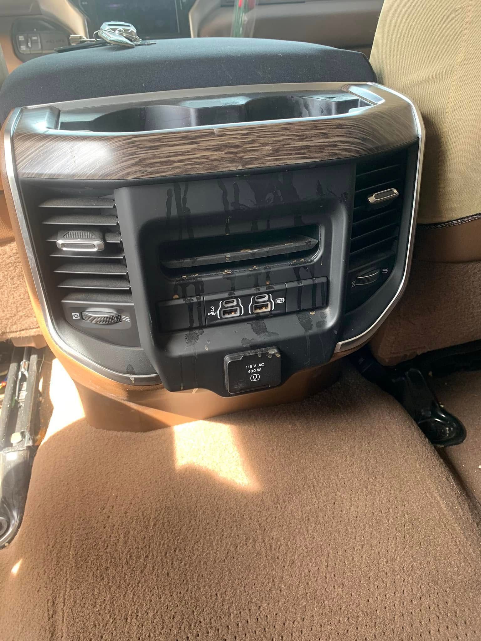 Center console with built-in car entertainment and climate controls, black with woodgrain trim and a brown seat below
