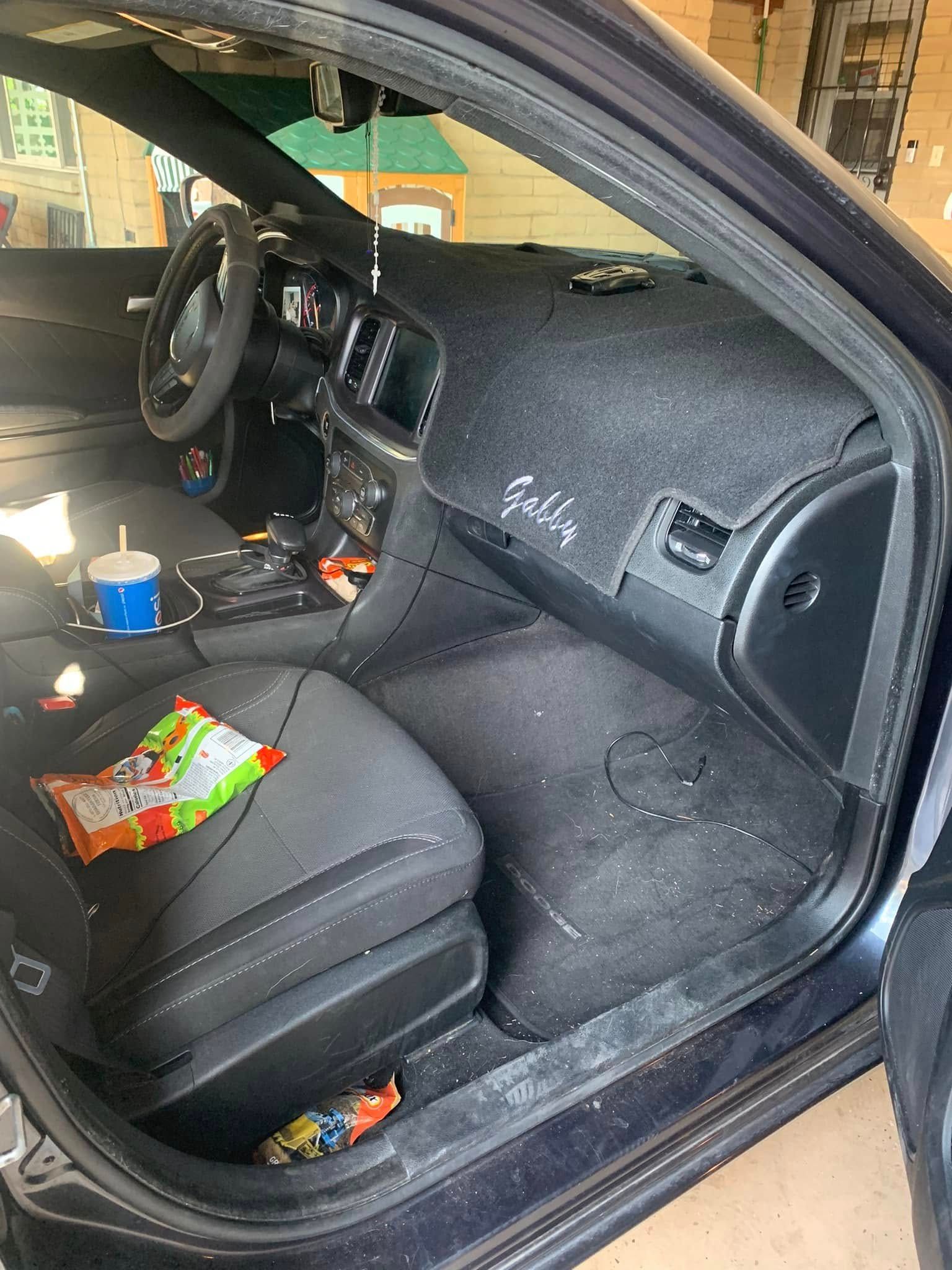 Car interior with clutter on the passenger floor and seat, including snacks and cups.