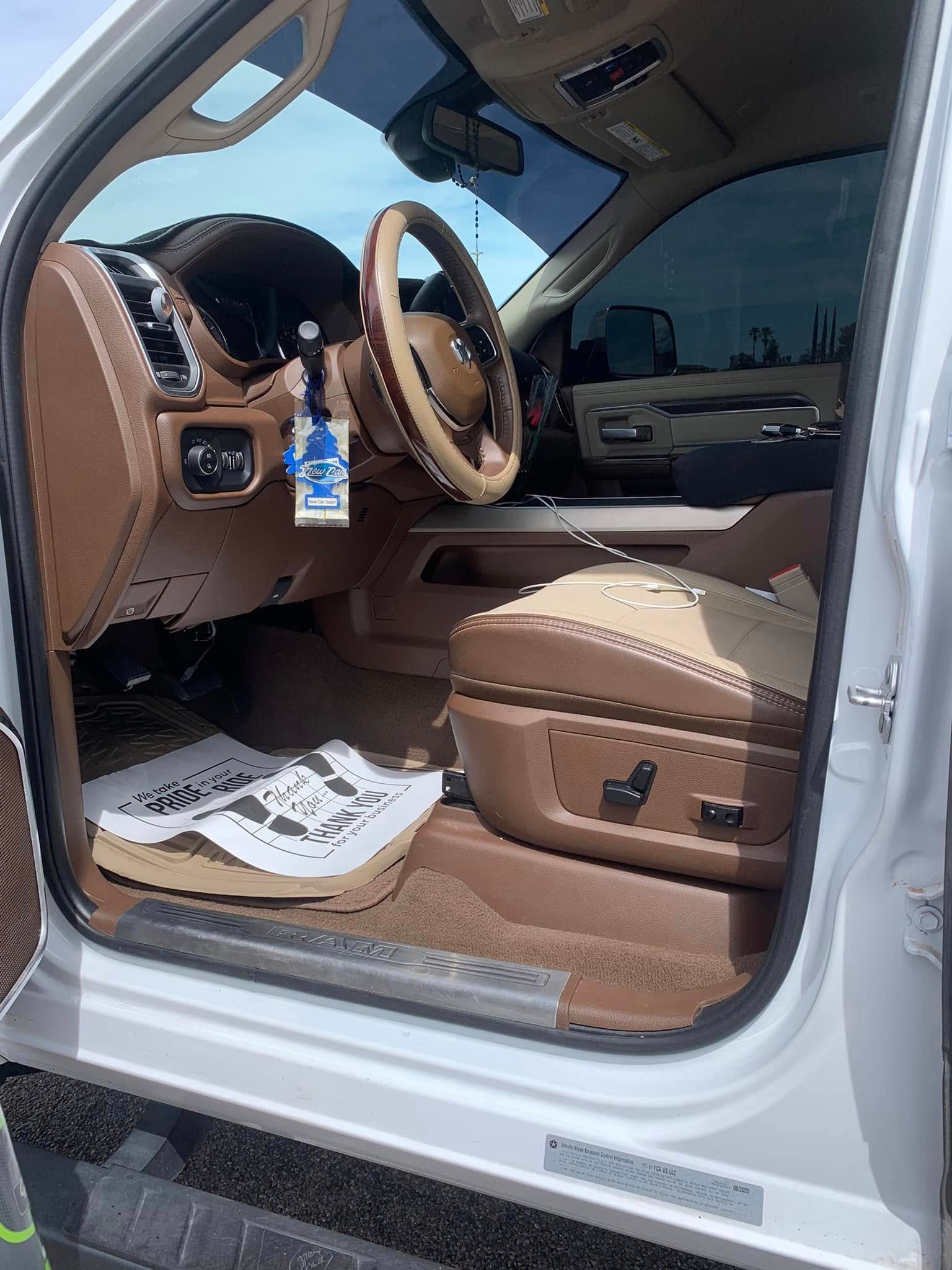 Tan leather car interior with open driver door, steering wheel, dashboard, and white floor mats.