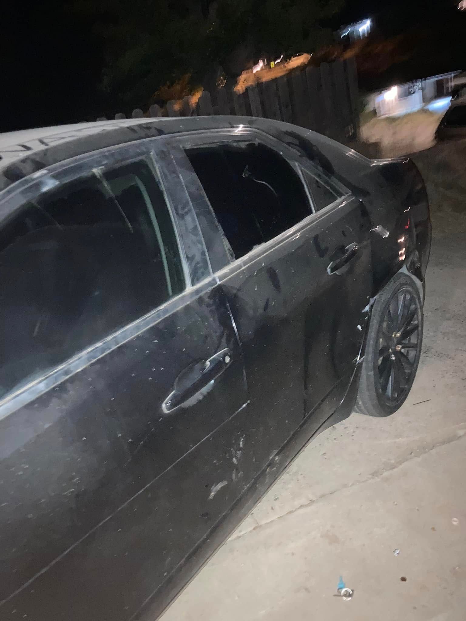 Black car parked at night on a driveway, with tinted windows and dark wheels.