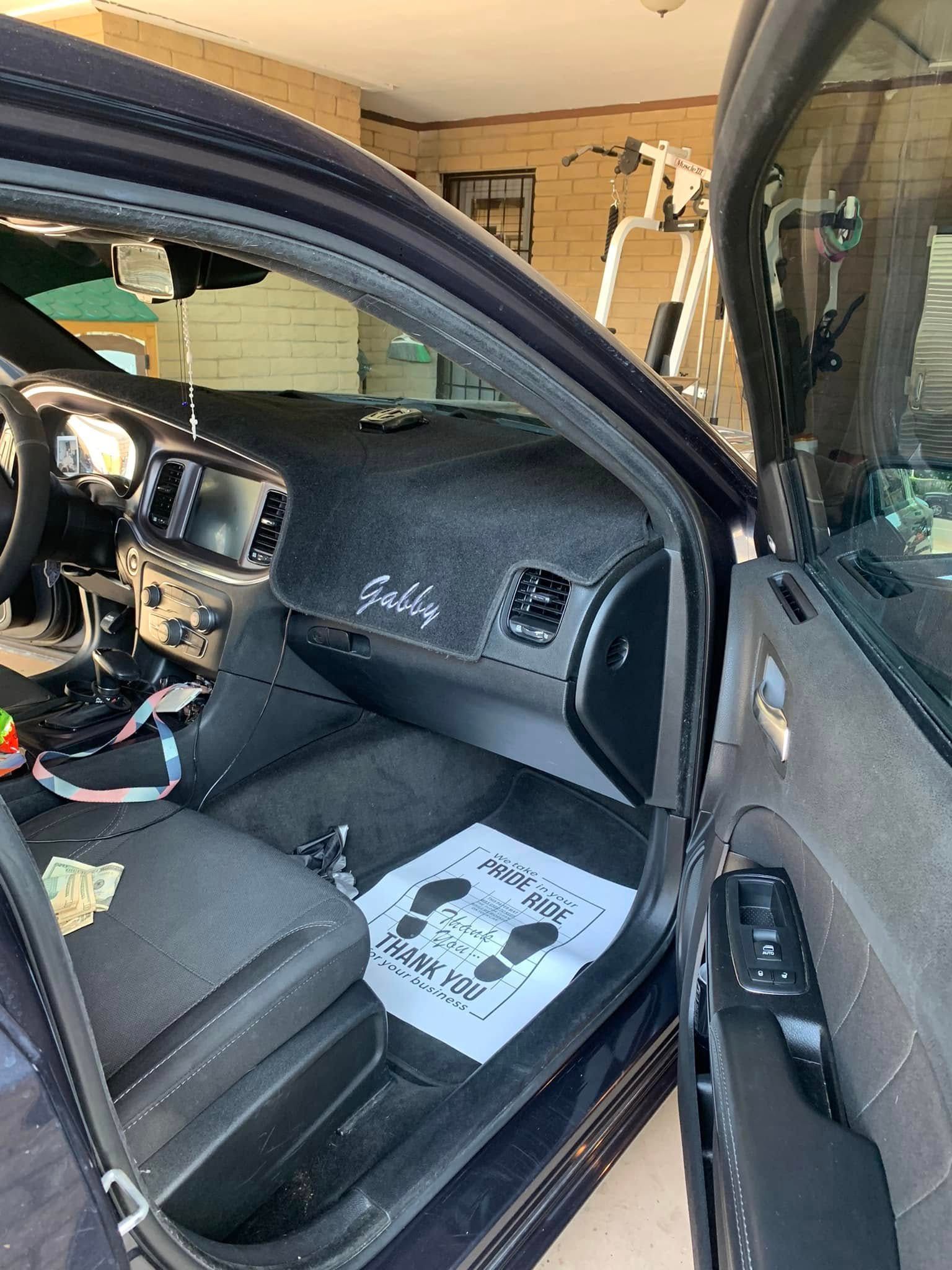 Open car door showing a black interior with an airbag deployment and a floor mat on the seat.