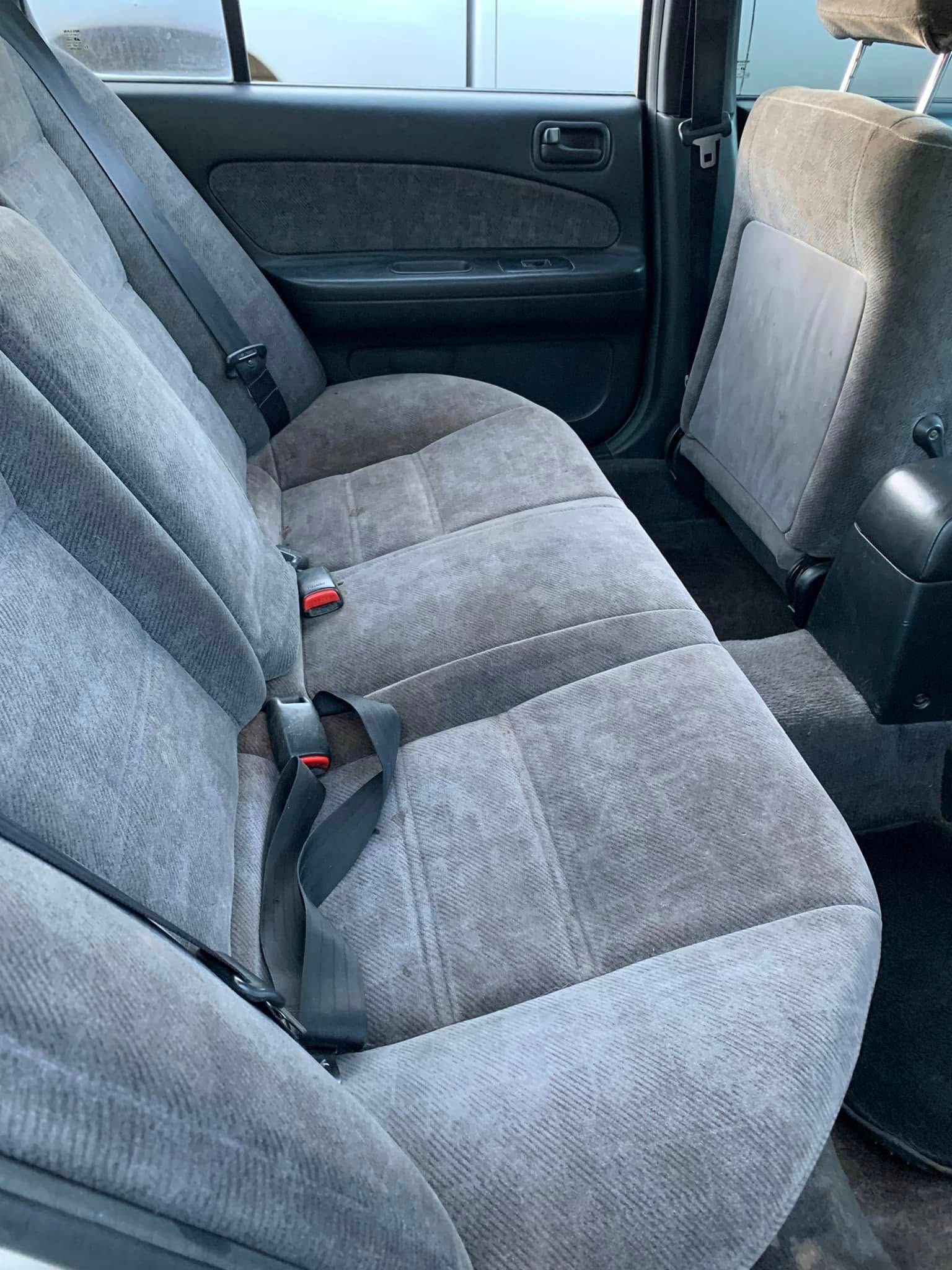 Gray cloth car back seat with three seats and red seatbelt buckles, viewed from the side