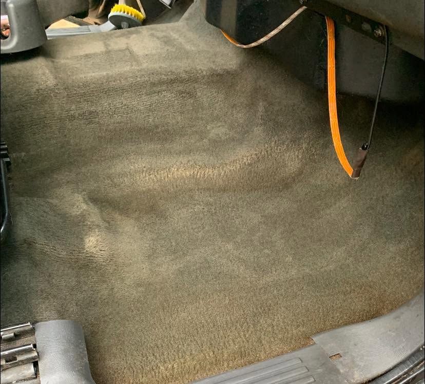Carpeted car floor with a hanging orange cable and gray plastic trim