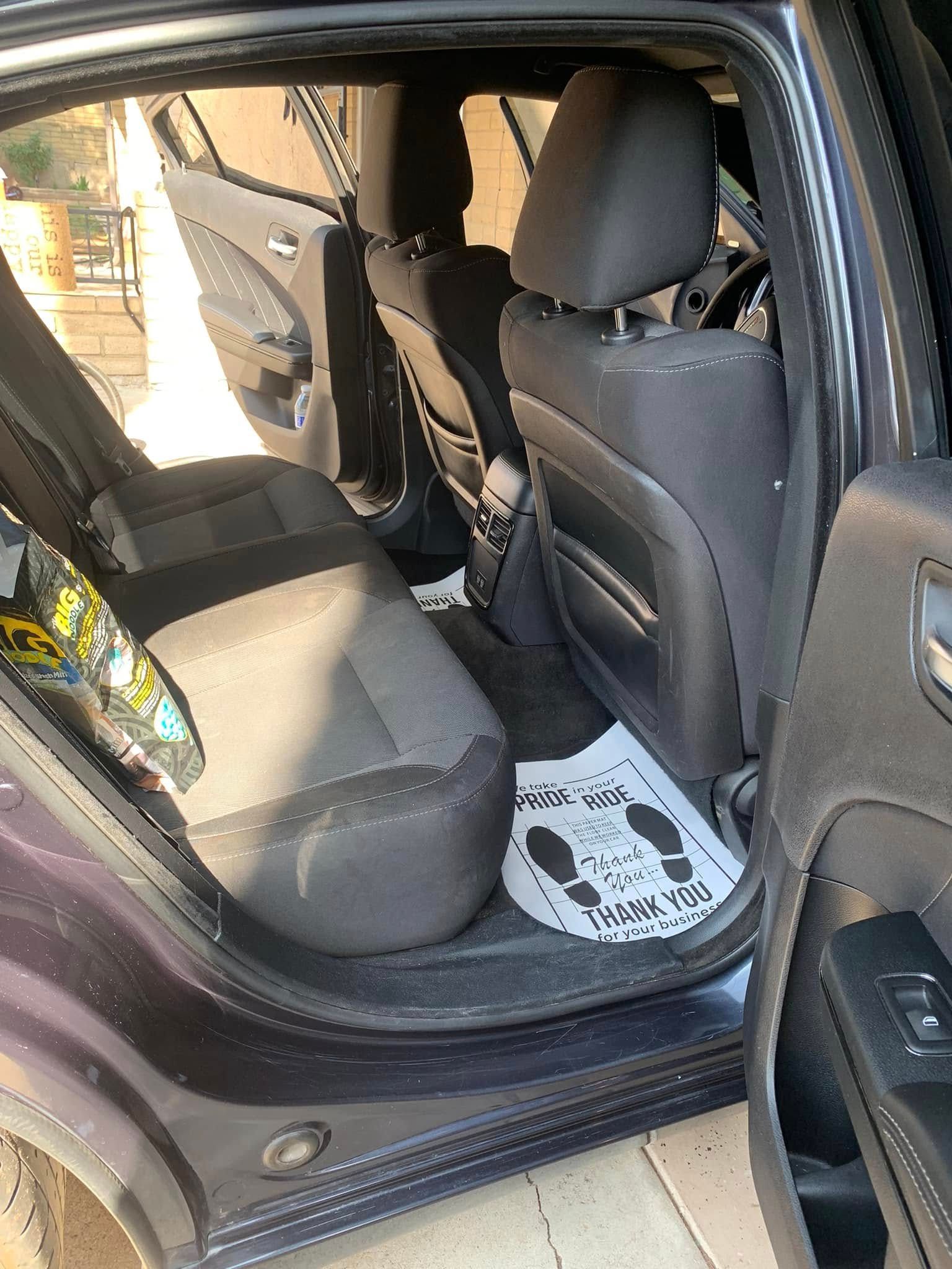 Open car rear door showing gray back seat and white floor mat.