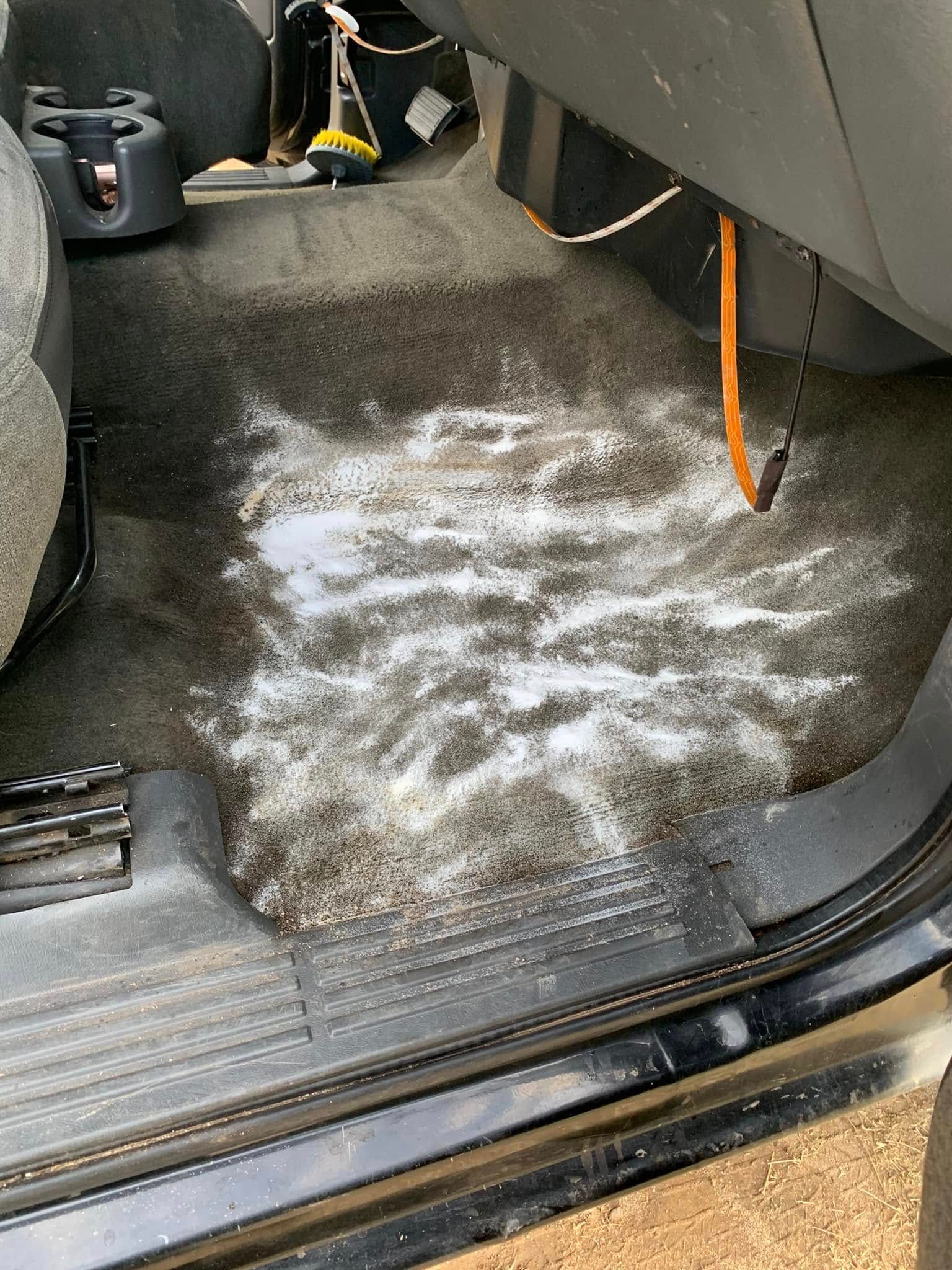 Car interior floor with a wet, dirty carpet and white residue near the driver’s footwell.