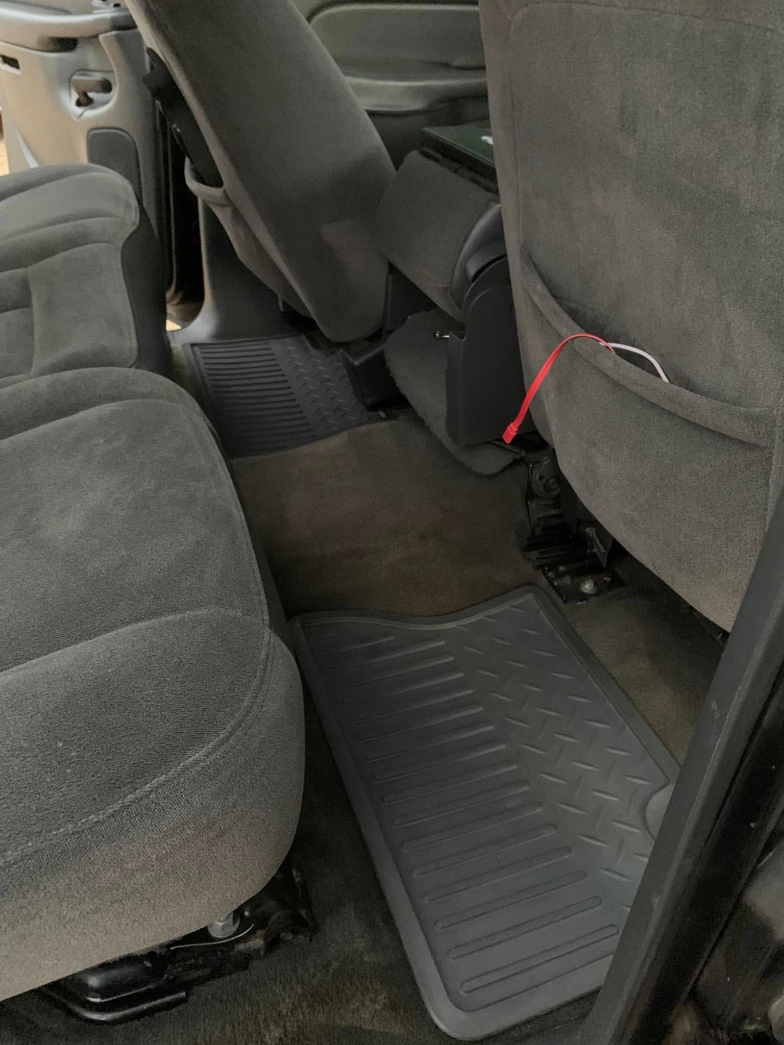 Rear car seat area with gray upholstery and a dark floor mat in the footwell