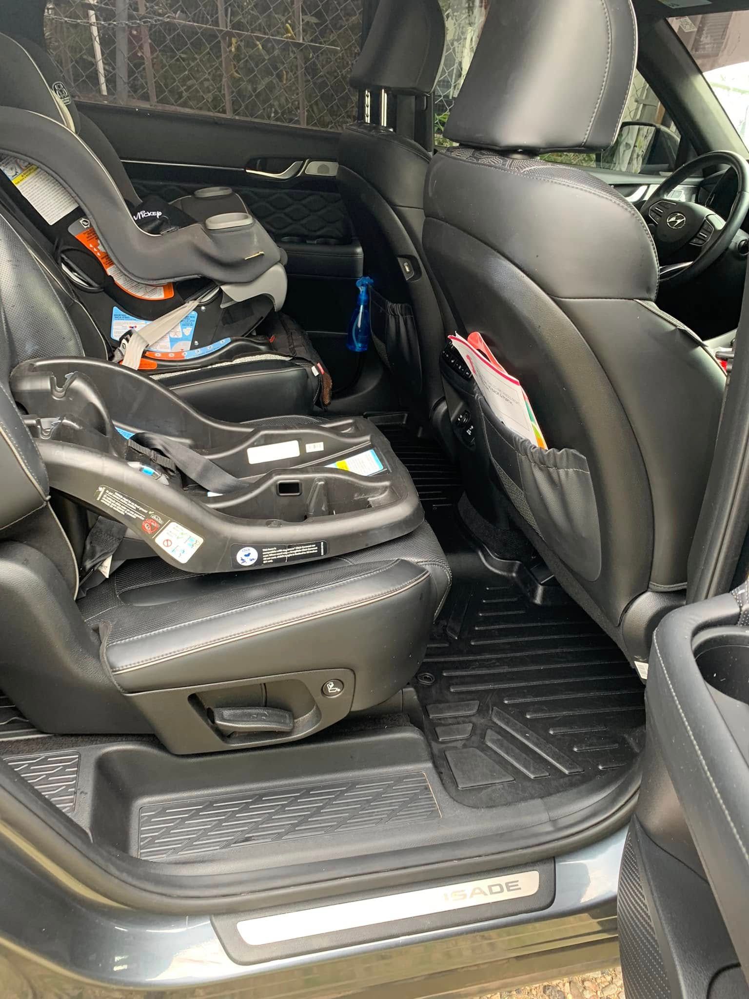 Three child car seats installed in the back row of a black SUV with a door open
