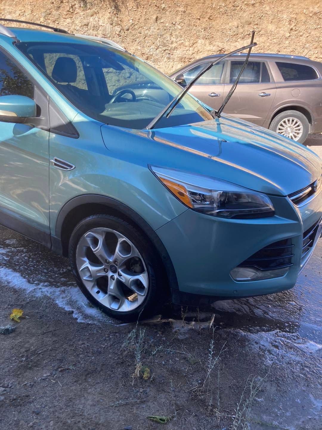 Blue compact SUV with windshield wipers raised, parked on a snowy street beside another car.