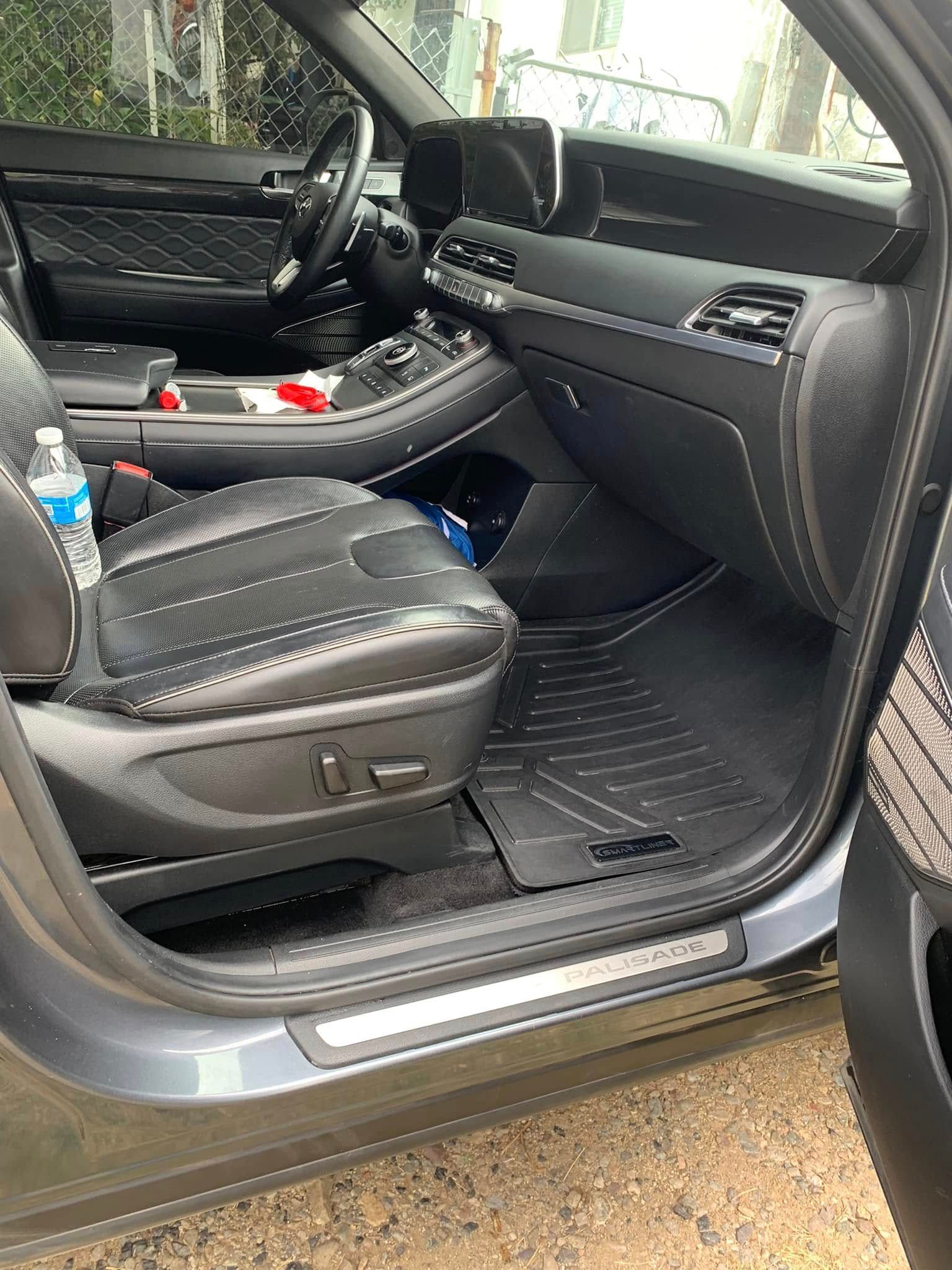 Open car door showing black leather front seat with controls and a floor mat inside.