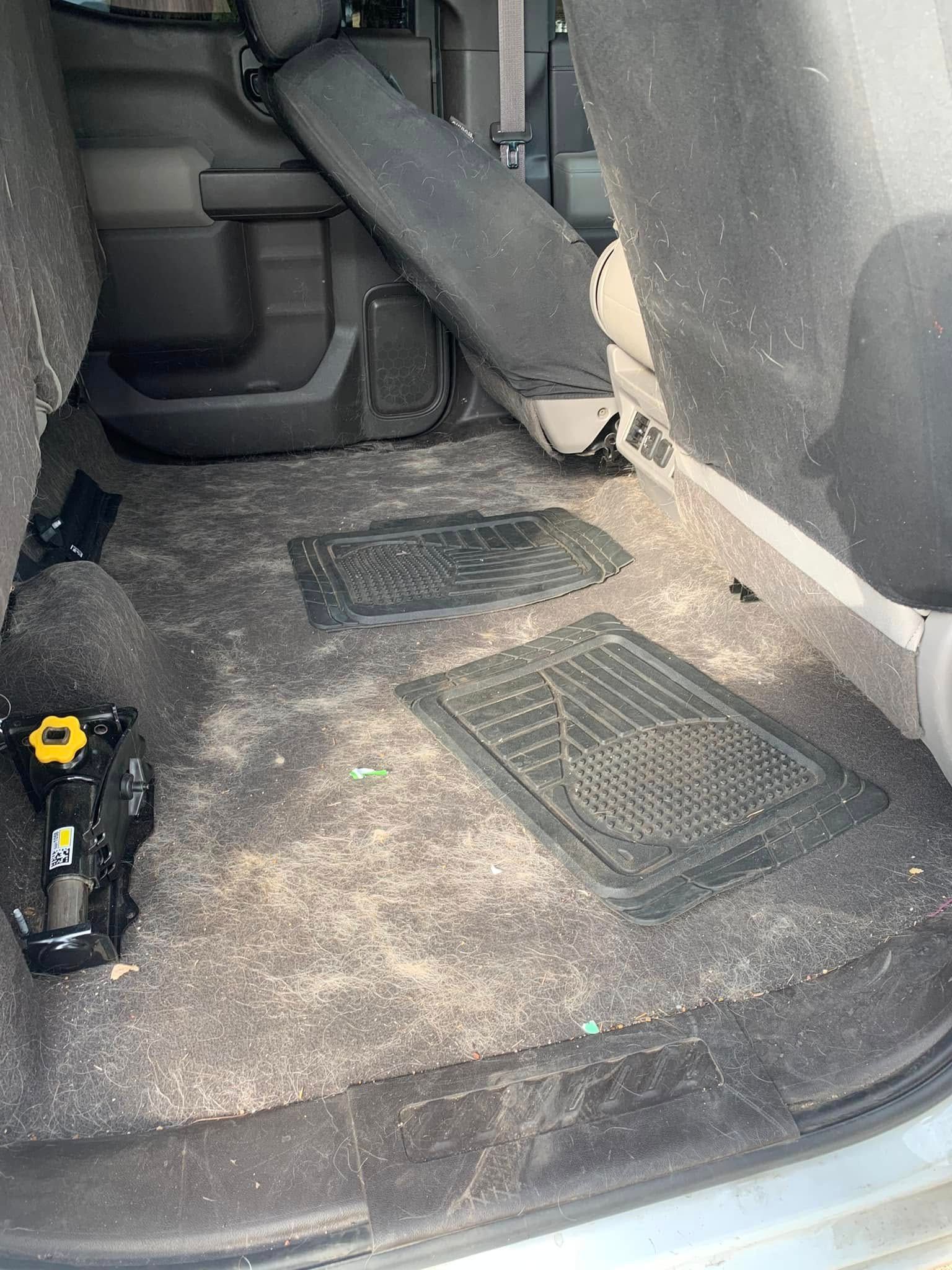 Dirty car trunk floor with loose floor mats and a small tool on the left side.