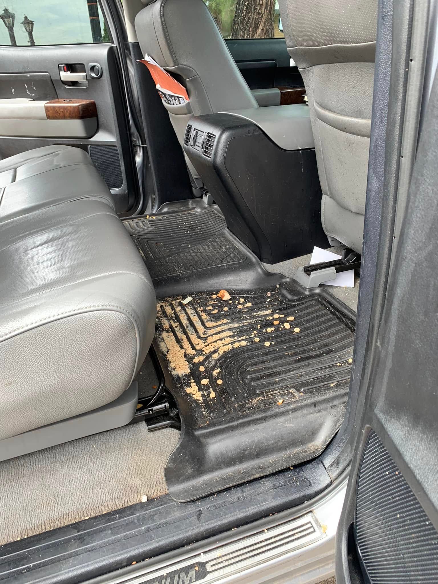 Car seat with a black step/cover and tan debris on a dirty floor mat inside a vehicle