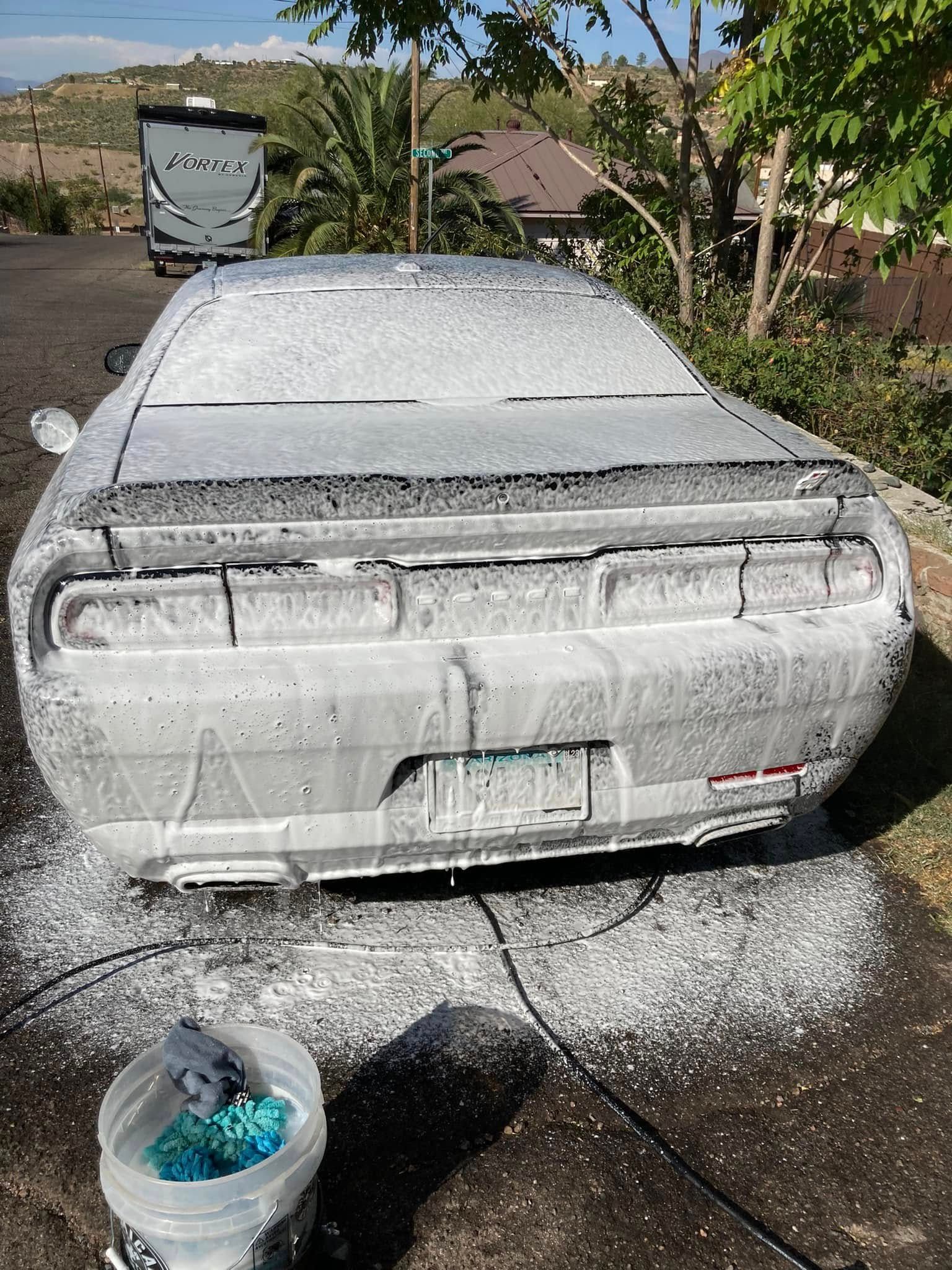 Snow-covered gray car in a driveway, with a bucket of blue water in the foreground.