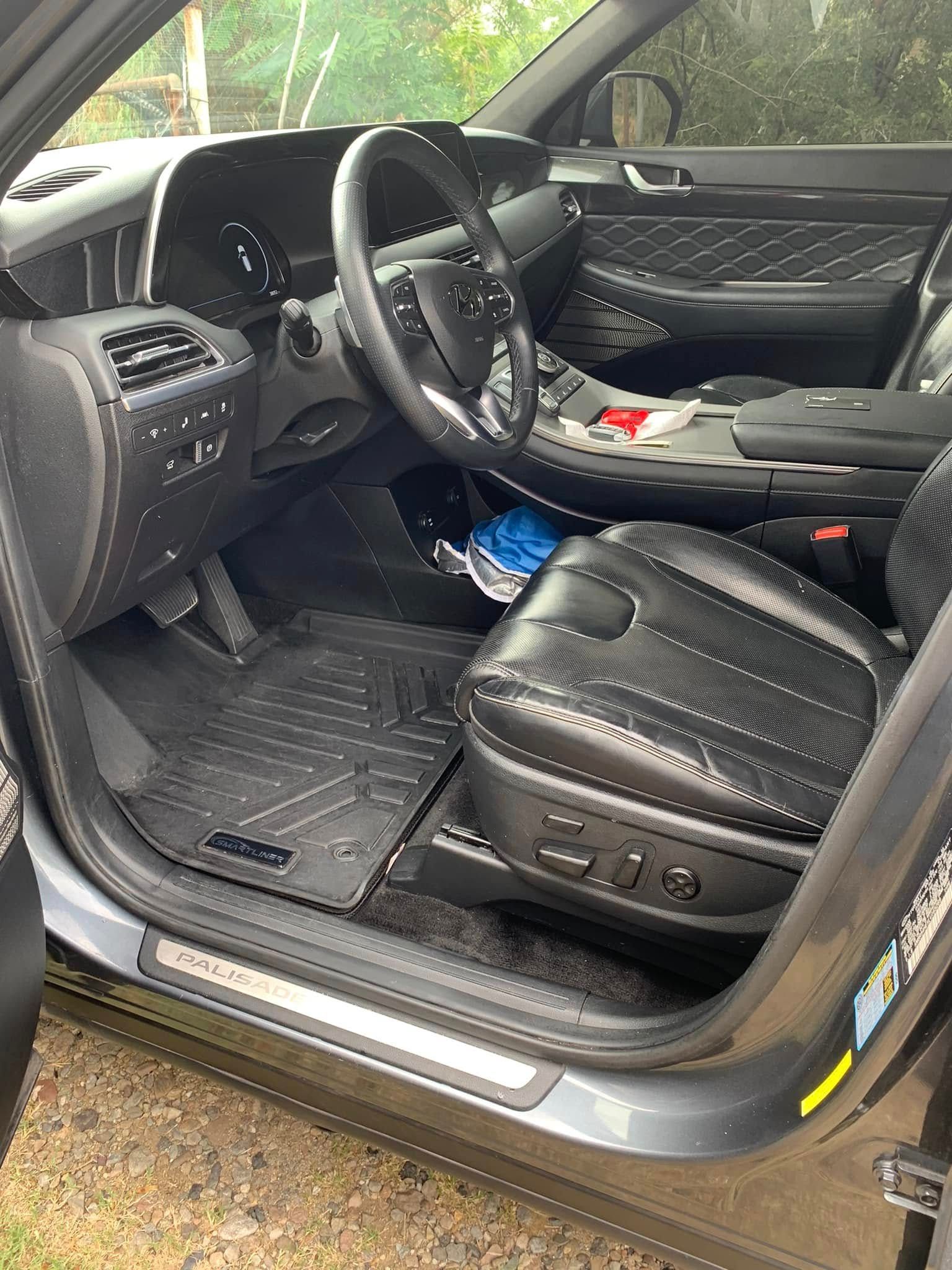 Black leather car interior with open driver door, steering wheel, and front seat controls visible