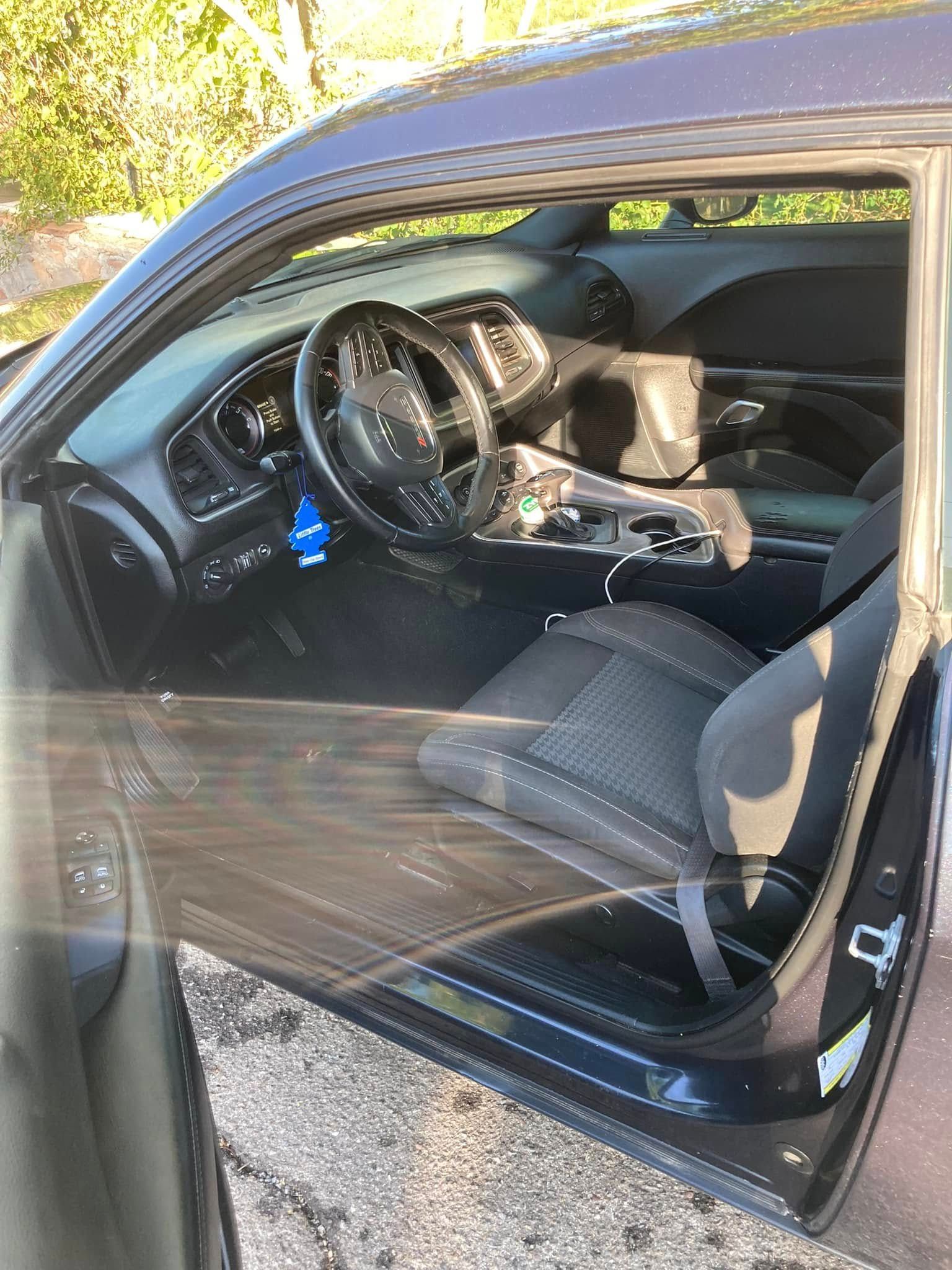Open car door showing black interior with steering wheel and front seat in sunlight
