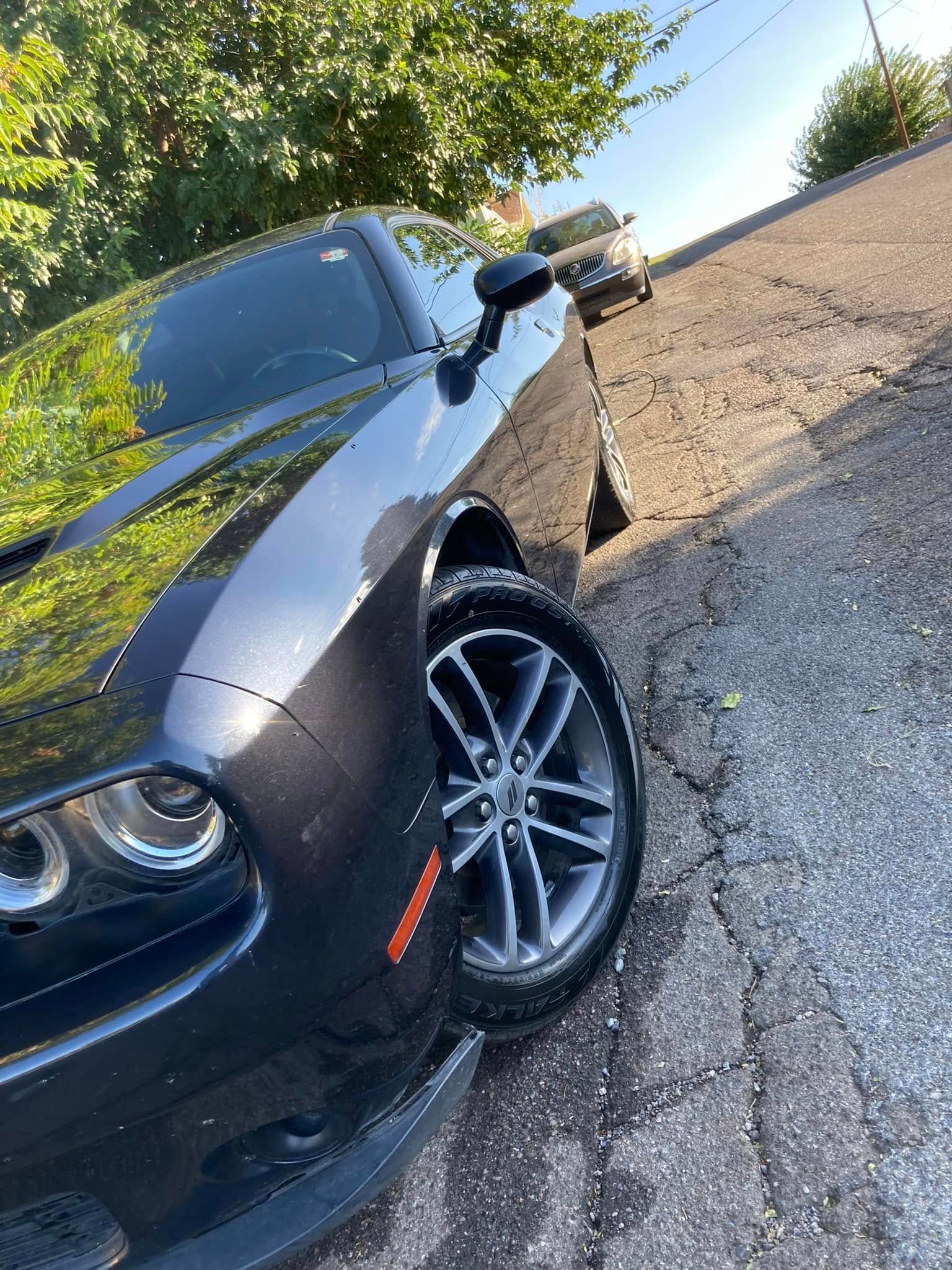 Black sports car parked on a roadside, front-left view, with a tree-lined background.