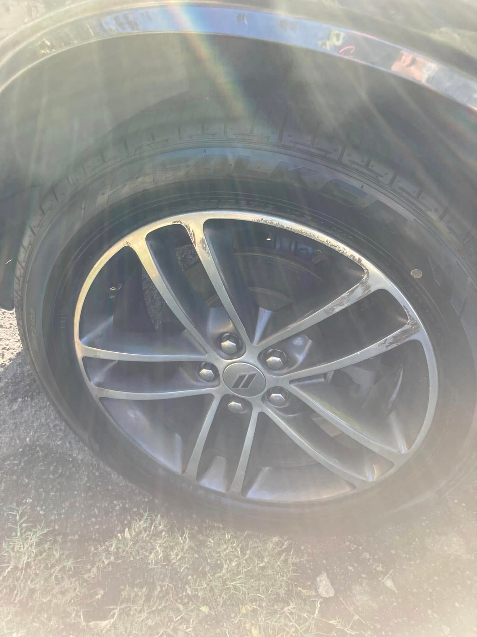 Black alloy car wheel with a flat tire on a sunlit road